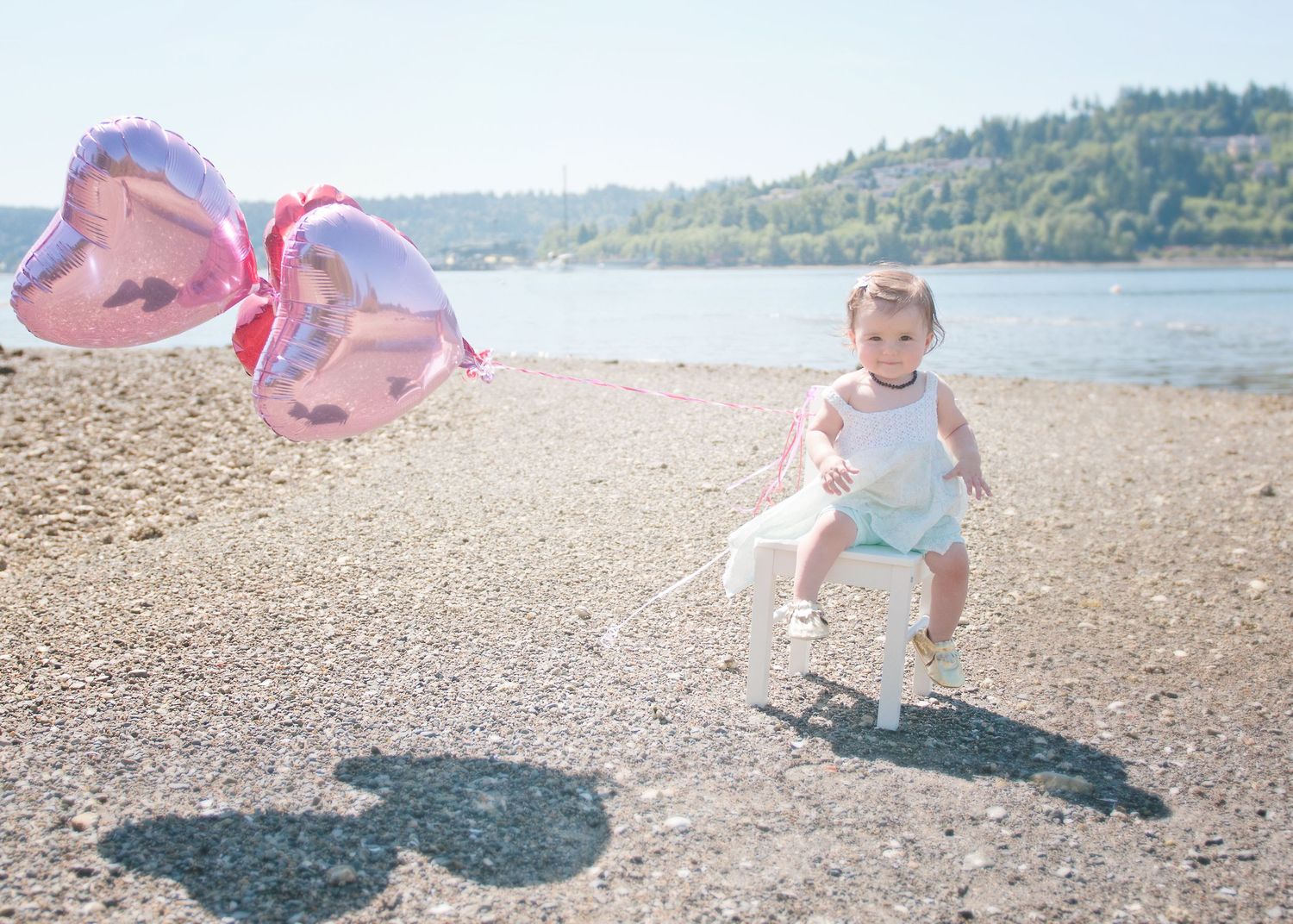 Whimsical beach photo with floating heart balloons casting shadows on pebbled shore.