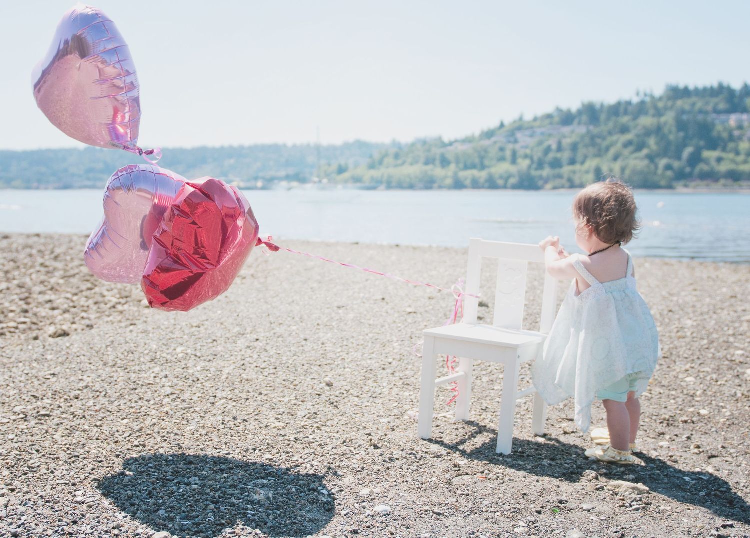 Ethereal beach scene with floating pink heart balloons and white furniture.