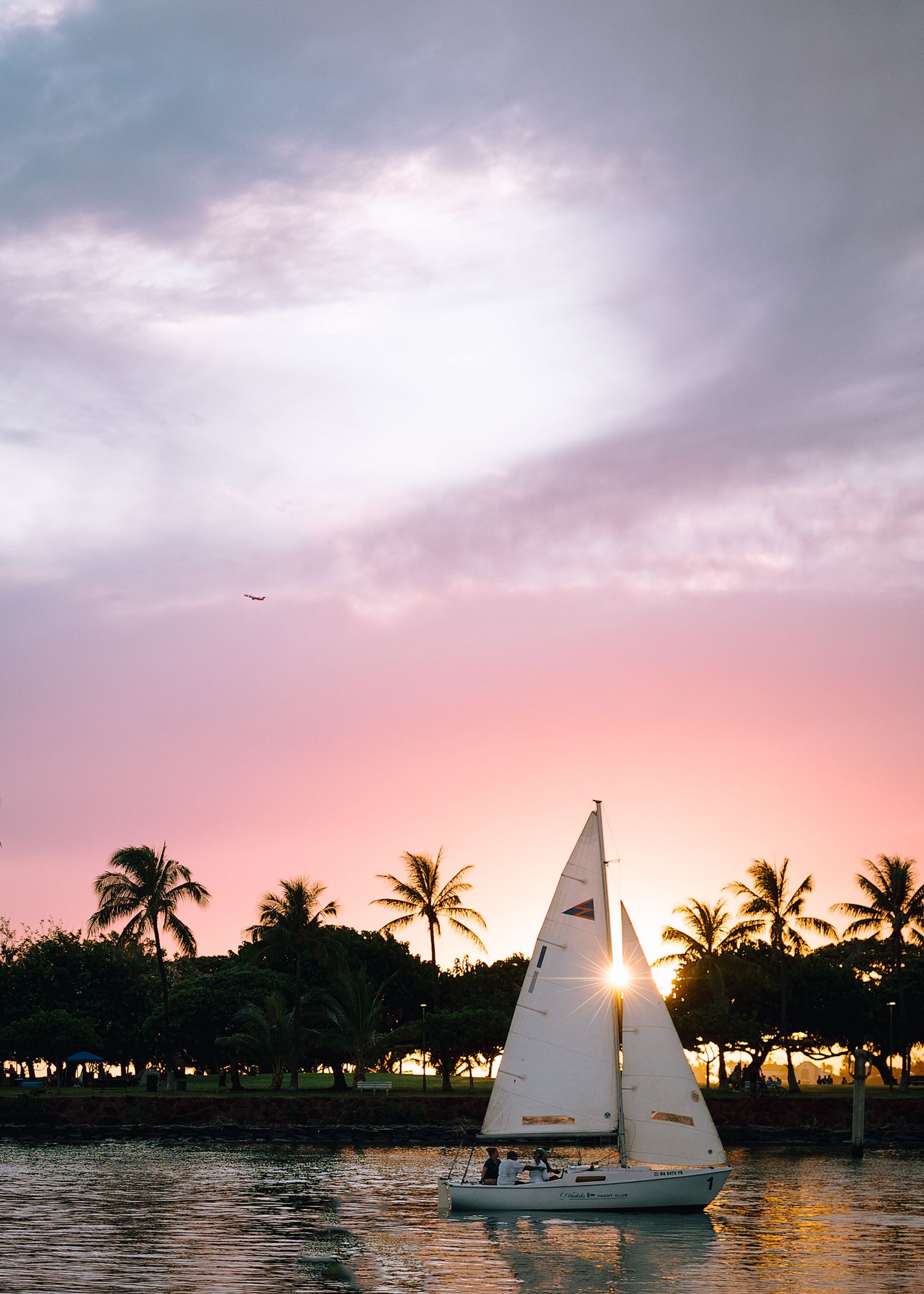 A small sailboat glides across calm waters during a vibrant pink sunset in Hawaii.