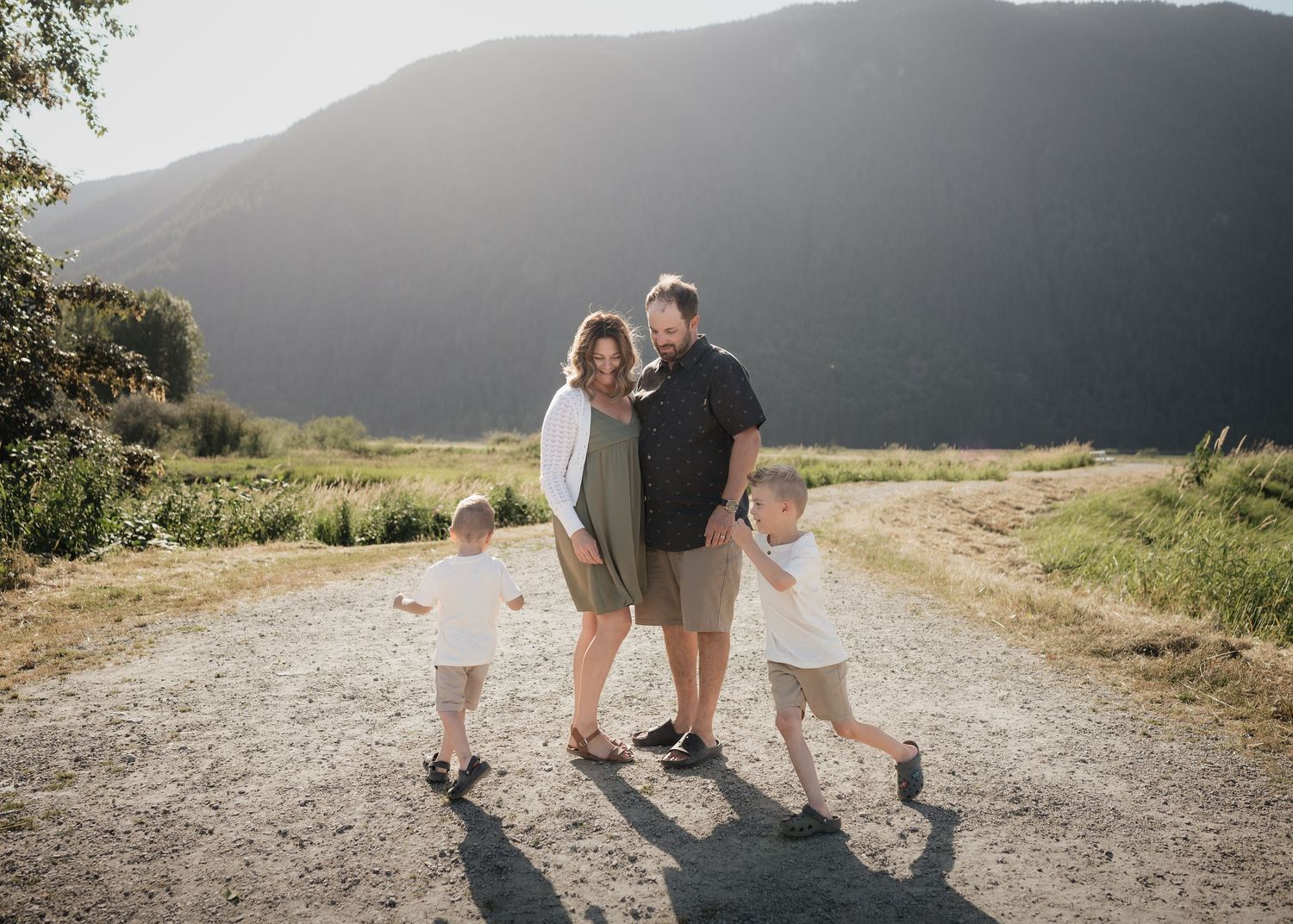 People walking together on a dirt path surrounded by mountains and fields during golden hour.