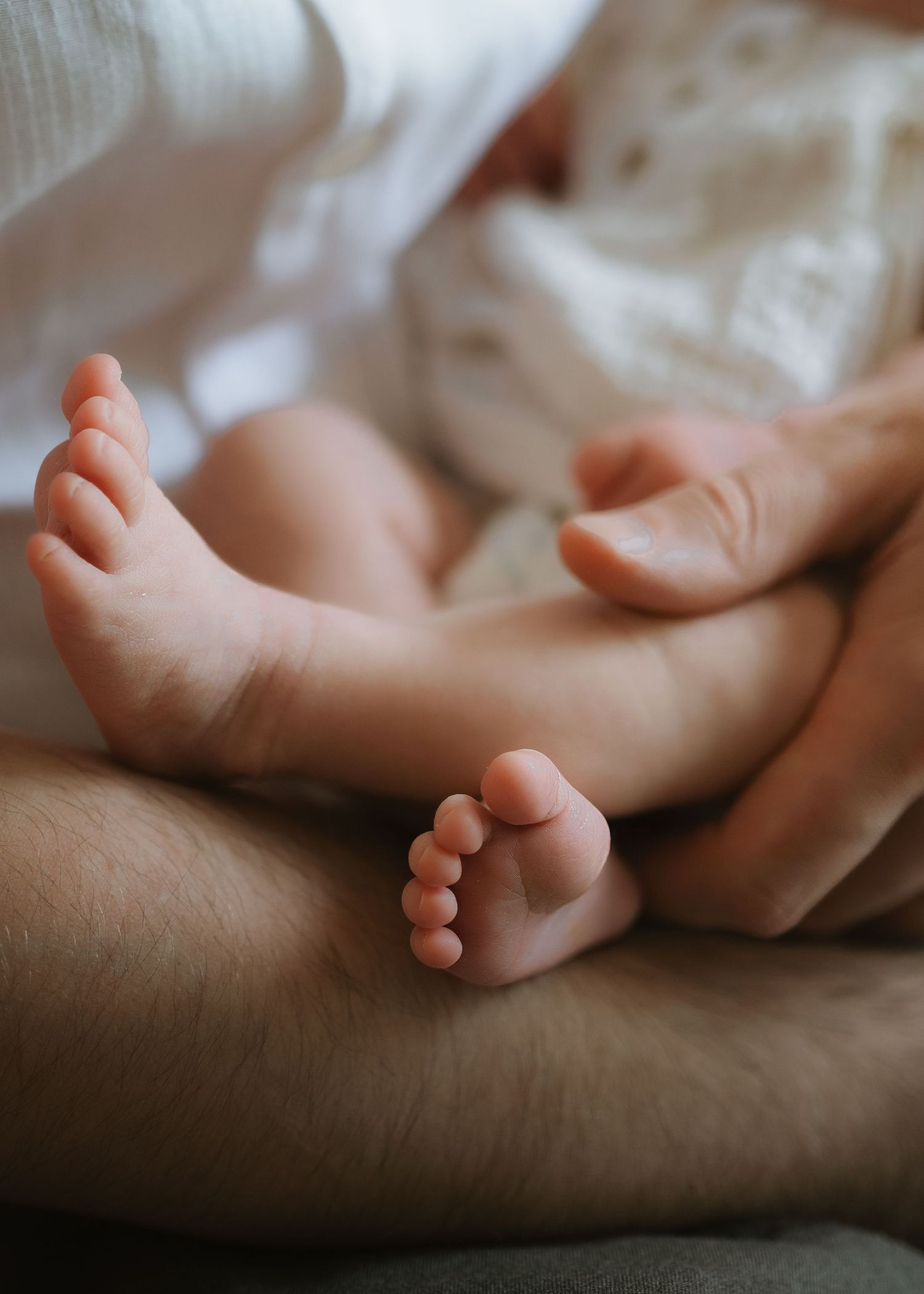 Close-up of a newborn baby's tiny feet resting on a father's arm as his hand gently cradles the infant.