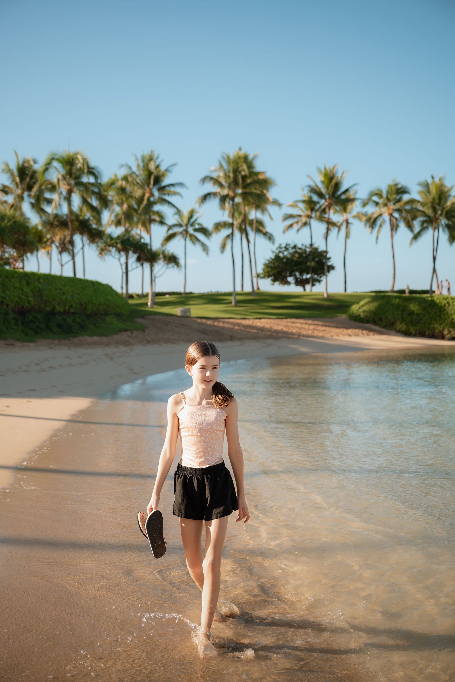 A scenic beach with palm trees lines the shore as a person splashes in the shallow tropical waters at sunset.