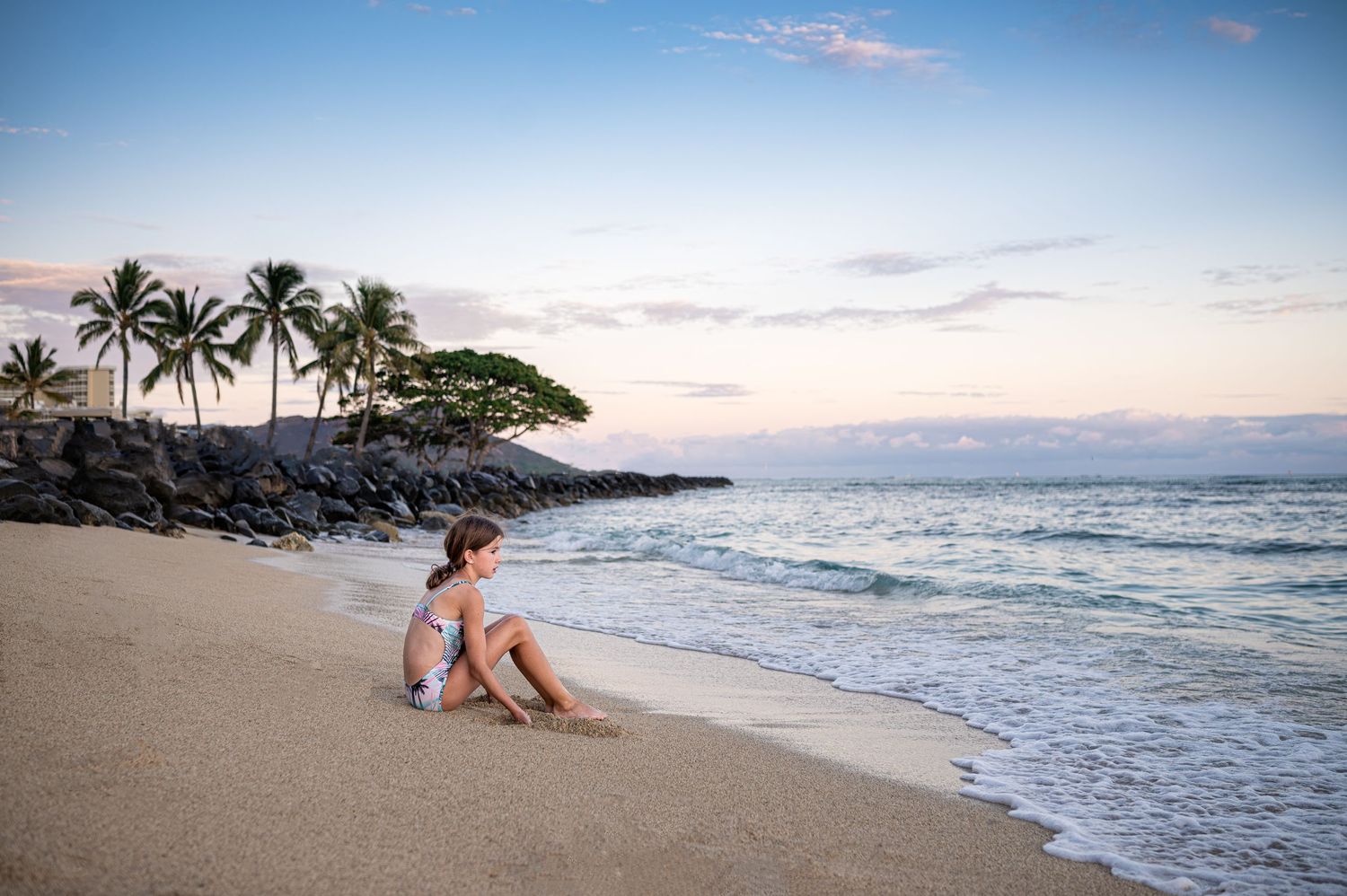A tranquil beach scene at sunset with palm trees and waves lapping at the shore.