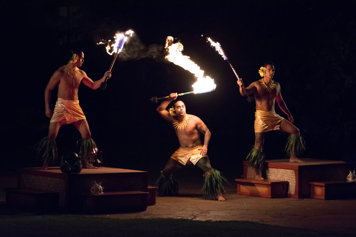 Fire dancers perform a mesmerizing routine on a dark stage with flaming props and dramatic lighting effects.