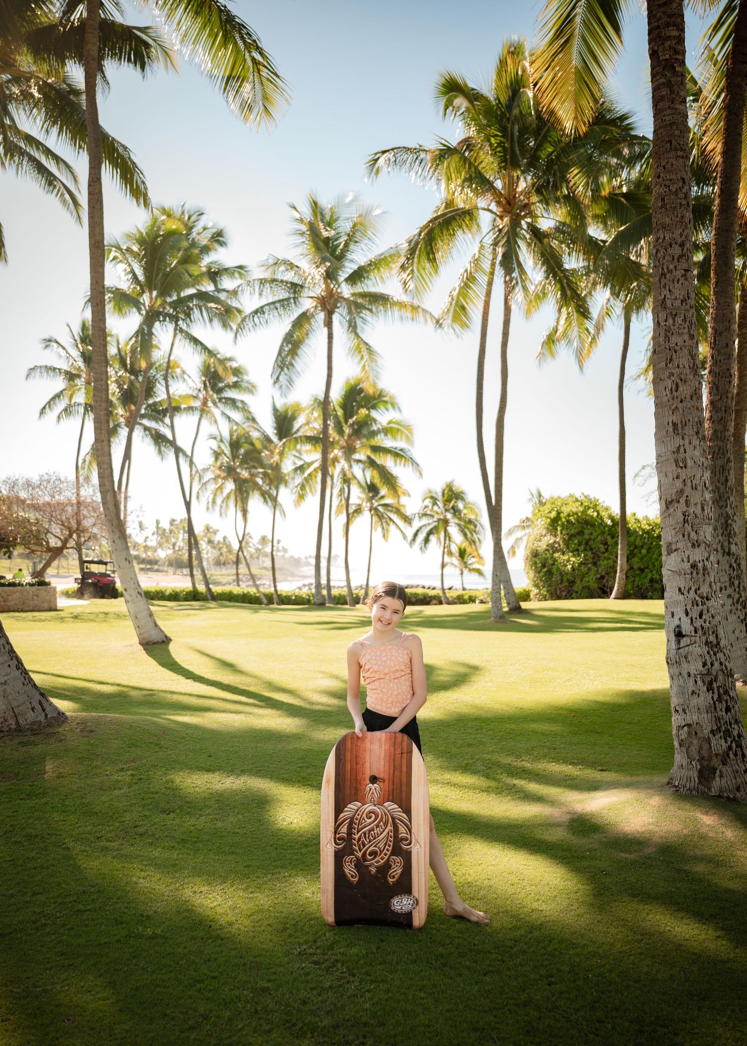 Person relaxing on a beach chair surrounded by palm trees on a manicured lawn at a tropical resort.