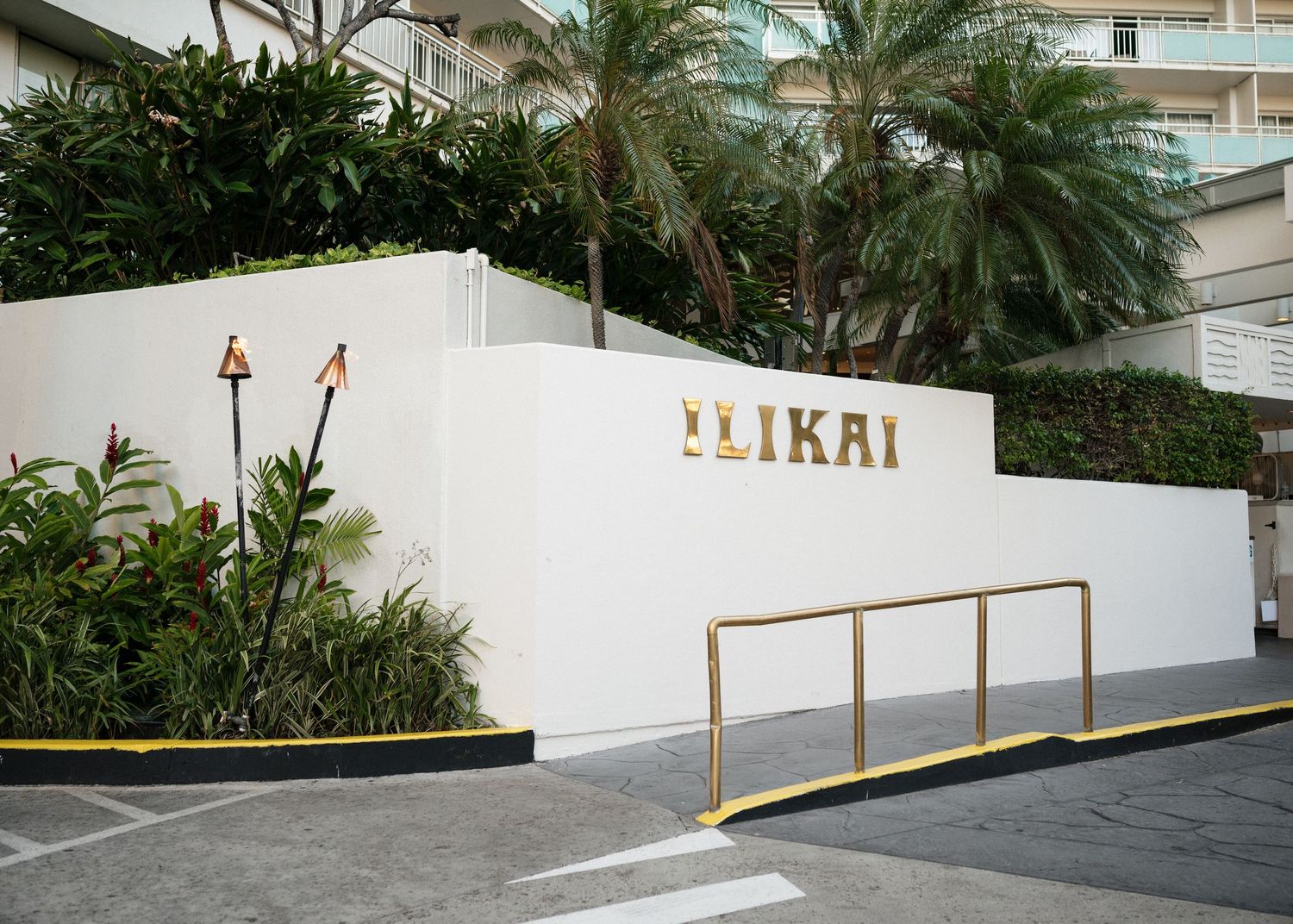 Modern white building entrance with Elikai sign and tropical landscaping.