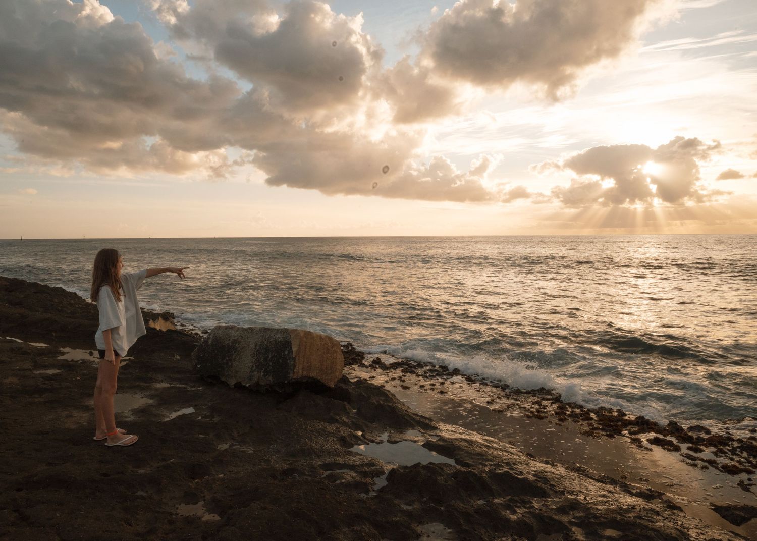 Dramatic sunset panorama over rocky Hawaiian coastline with crashing waves and golden clouds reflecting on ocean surface.