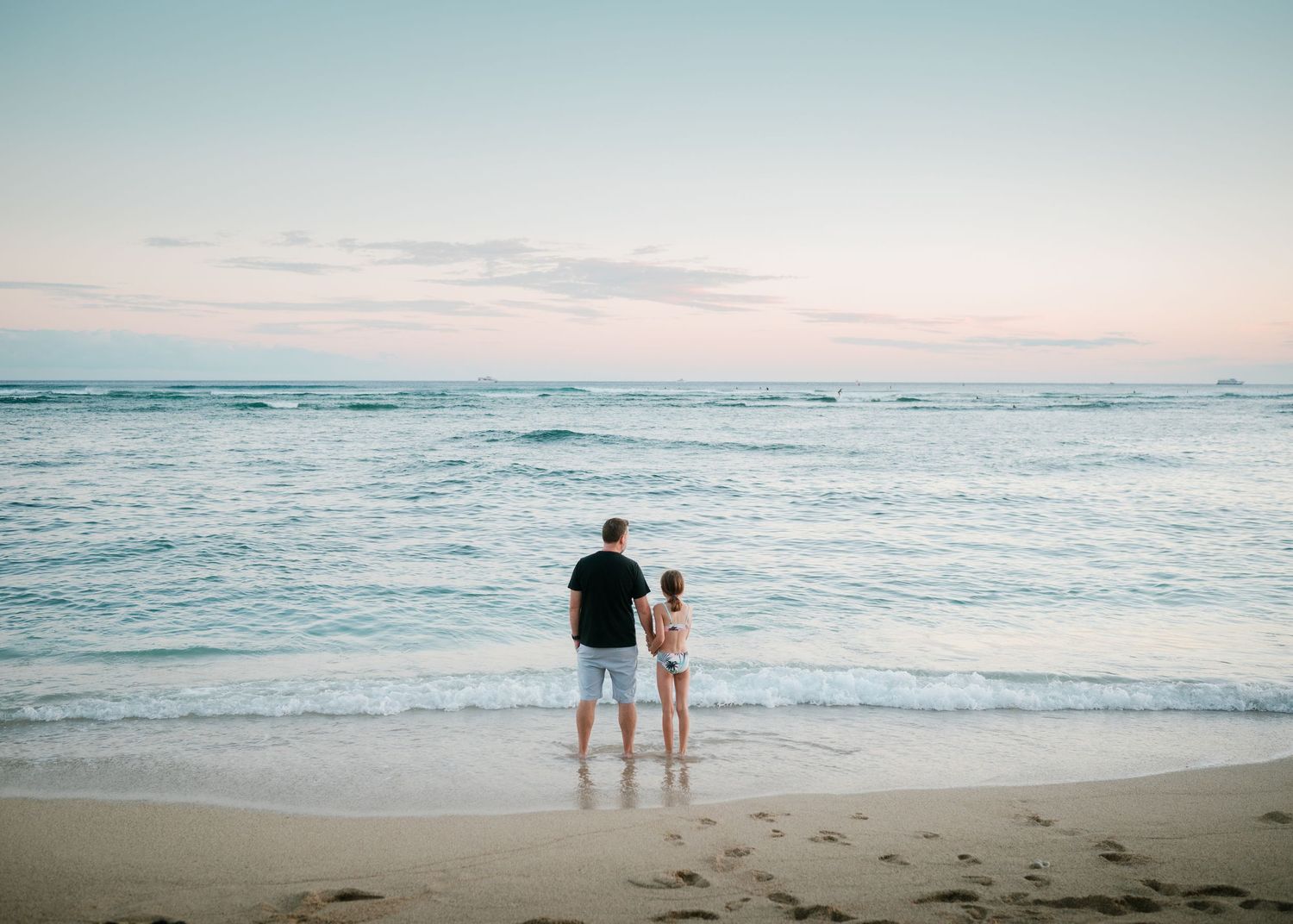 Two silhouettes stand together watching the sunset on a Hawaiian beach.