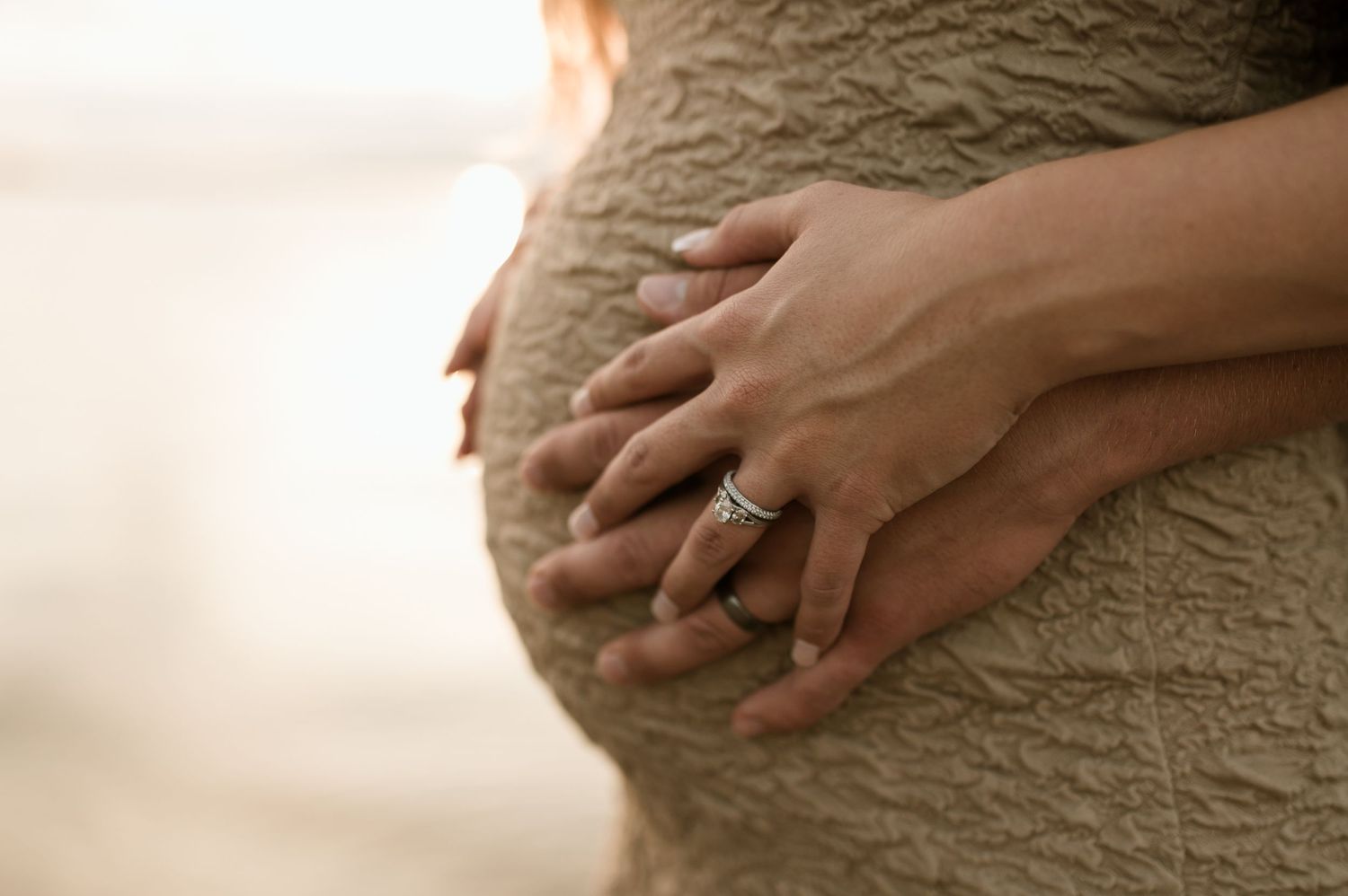 Close-up of a pregnant belly with couple's hands resting together, woman wearing diamond ring.