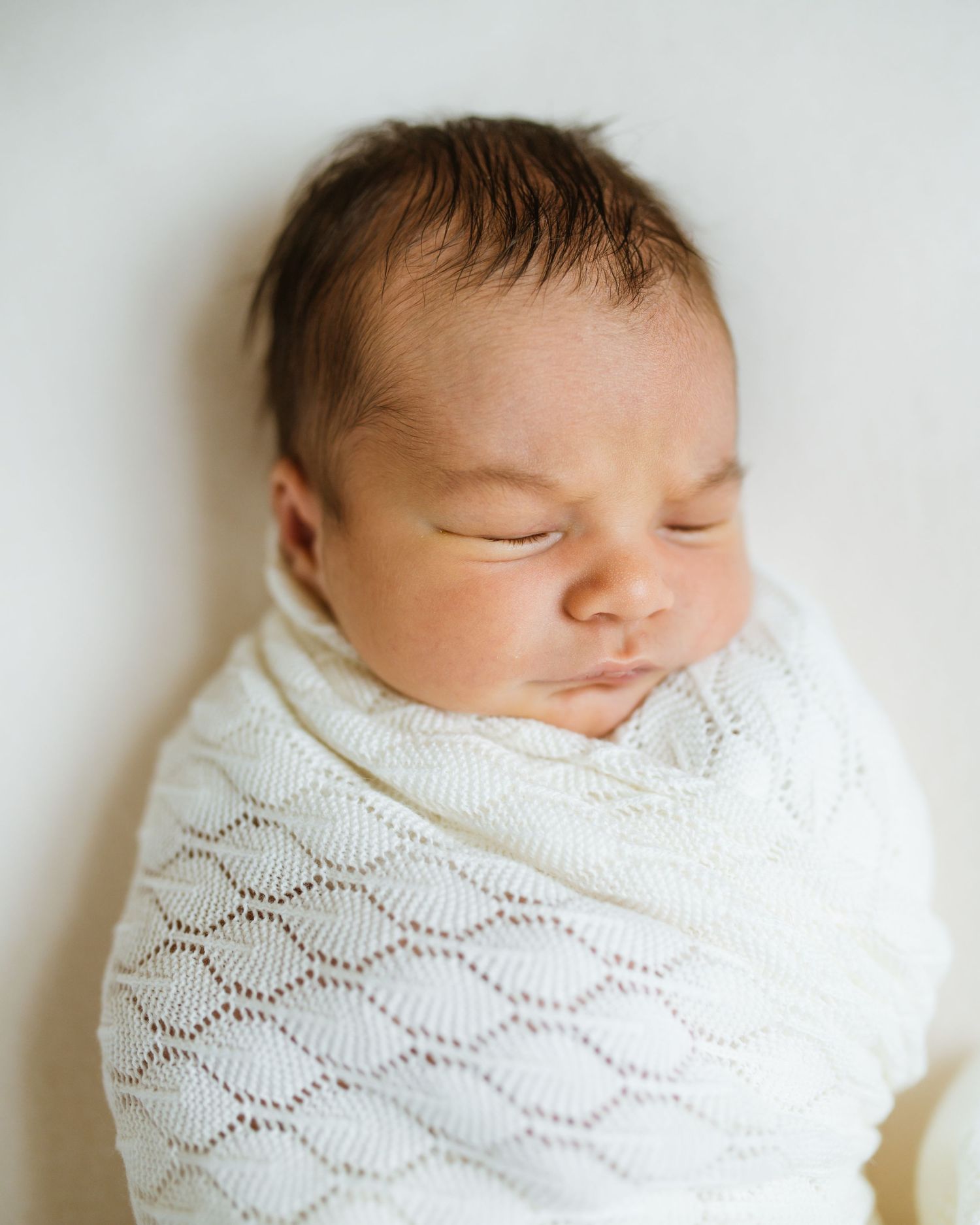 Sleeping newborn baby wrapped snugly in white knit swaddle blanket during professional newborn portrait session.