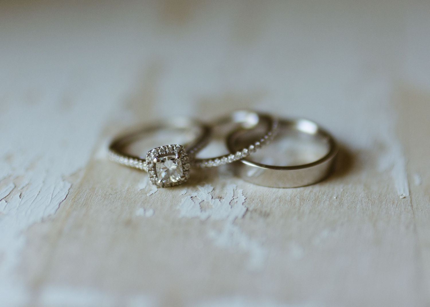 Three silver wedding rings with diamond halo engagement ring displayed on rustic white surface.