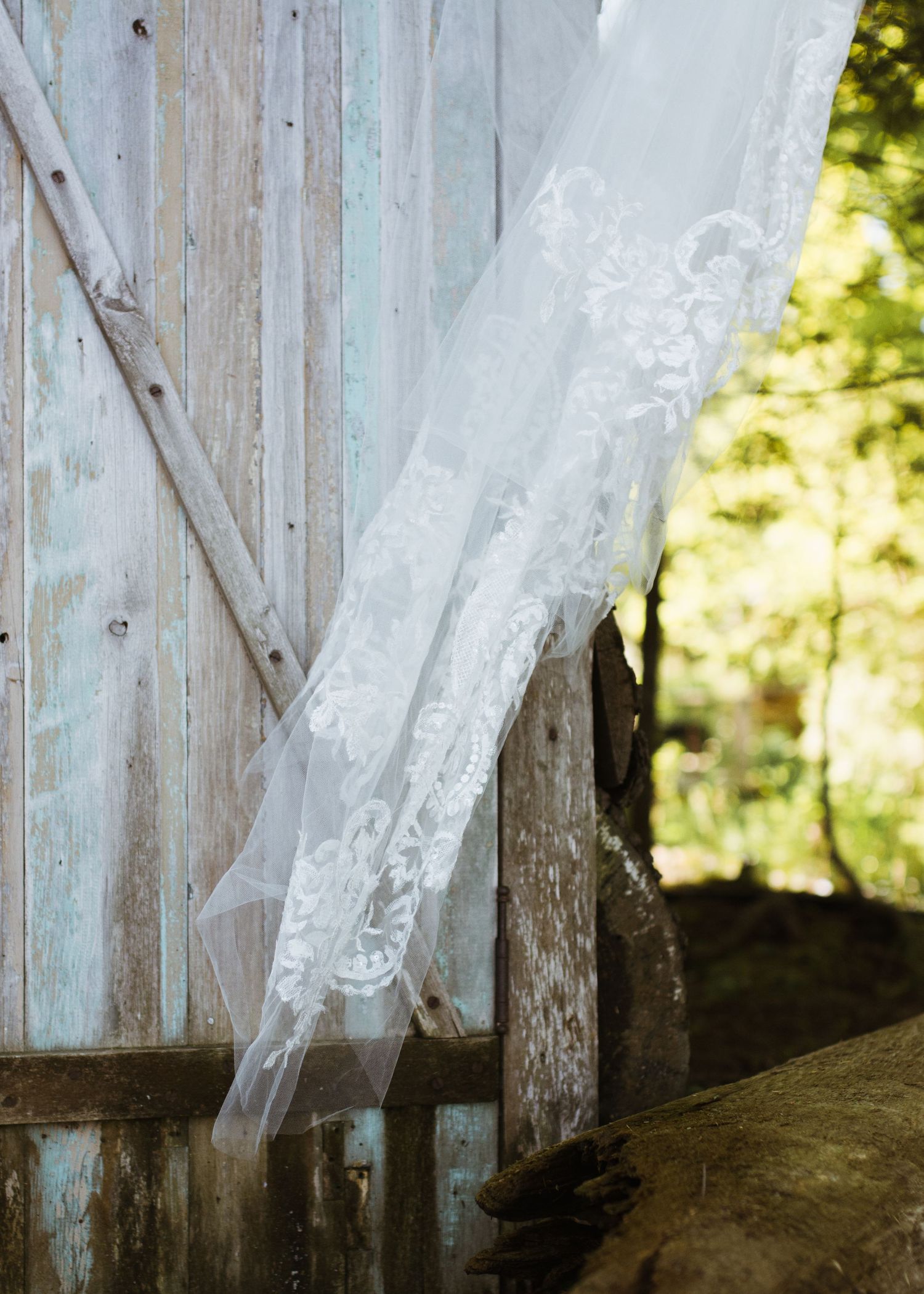 Elegant lace wedding veil draped against a rustic blue weathered barn wall outdoors.