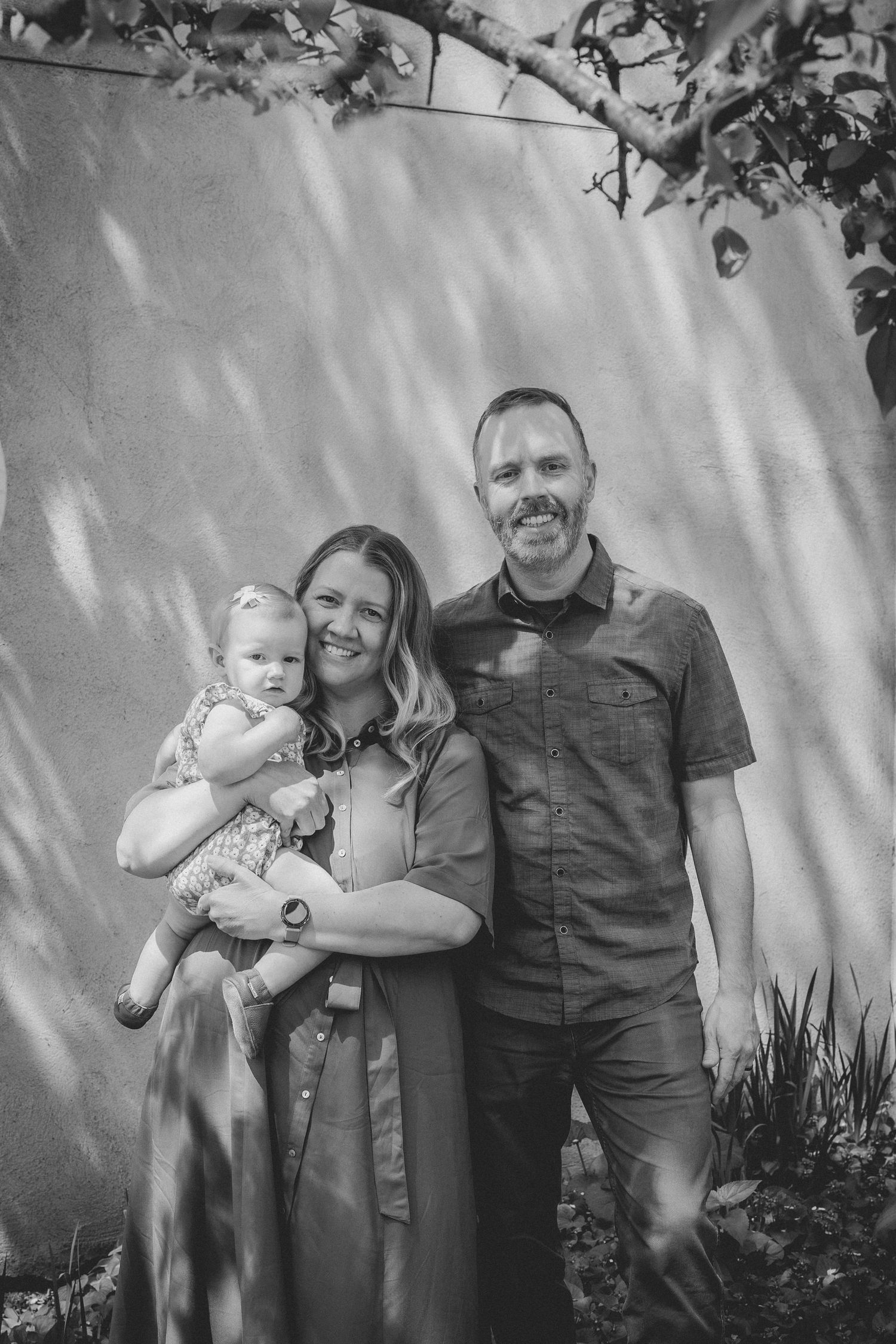 Black and white portrait of a happy family of three posing against a textured wall. Twin Cities Family Photographer.