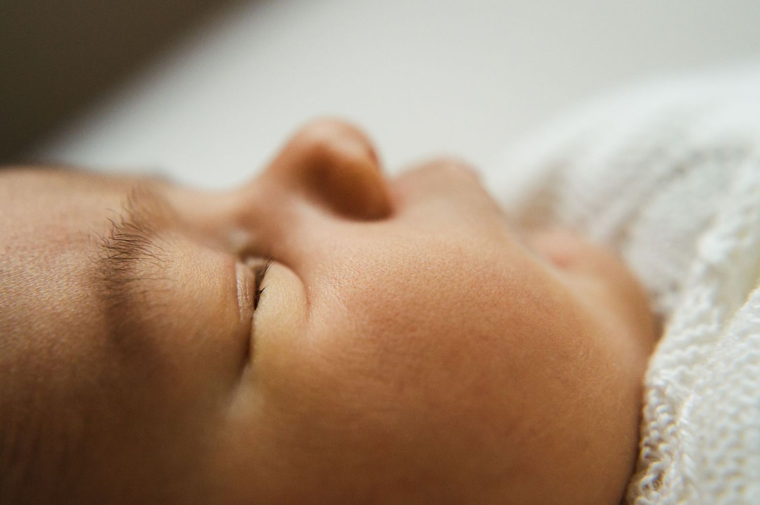 Extreme close-up of peaceful sleeping newborn baby's delicate facial features wrapped in white knit blanket.