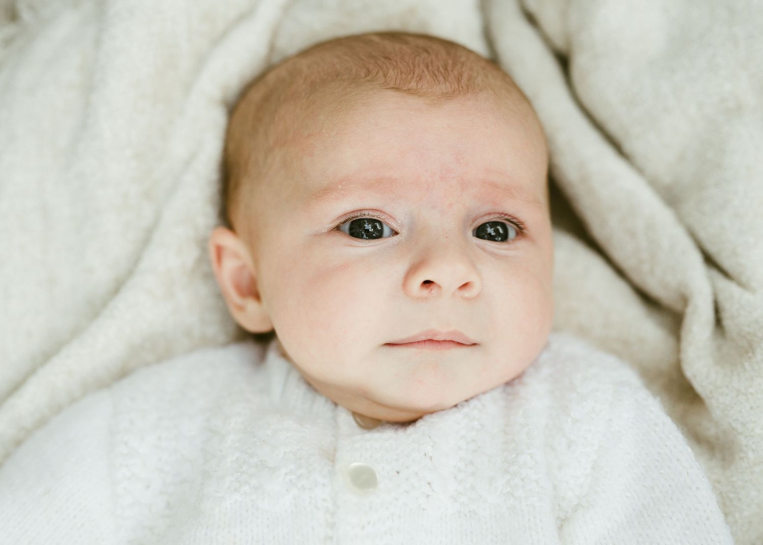Adorable newborn baby in white outfit lying on soft knit blanket.