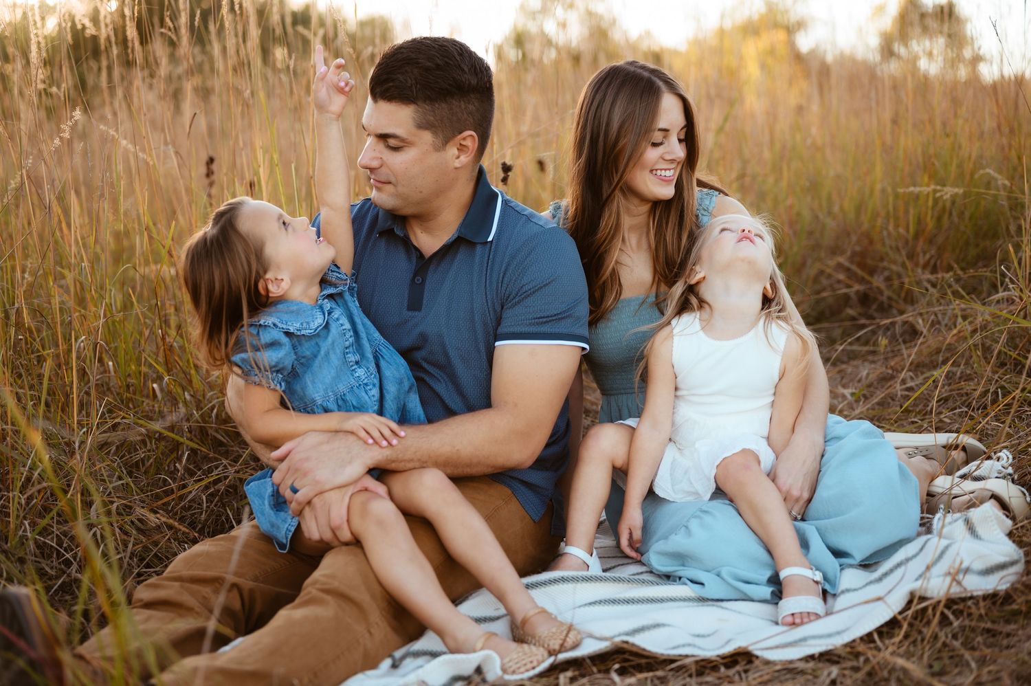 Young family relaxing on a blanket in a golden field, children playing with their parents.
