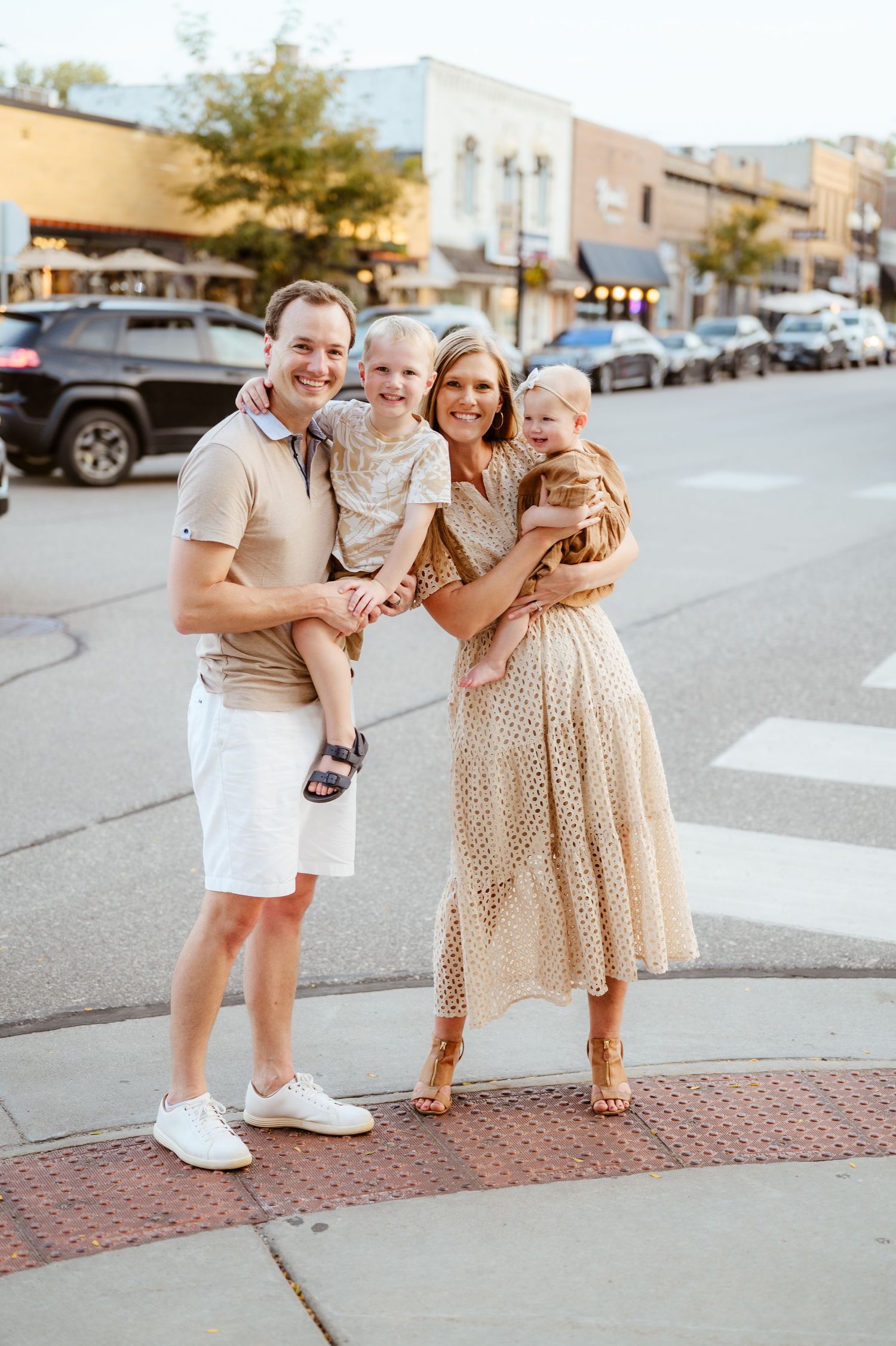 A smiling family of four poses together on a downtown street corner at golden hour.