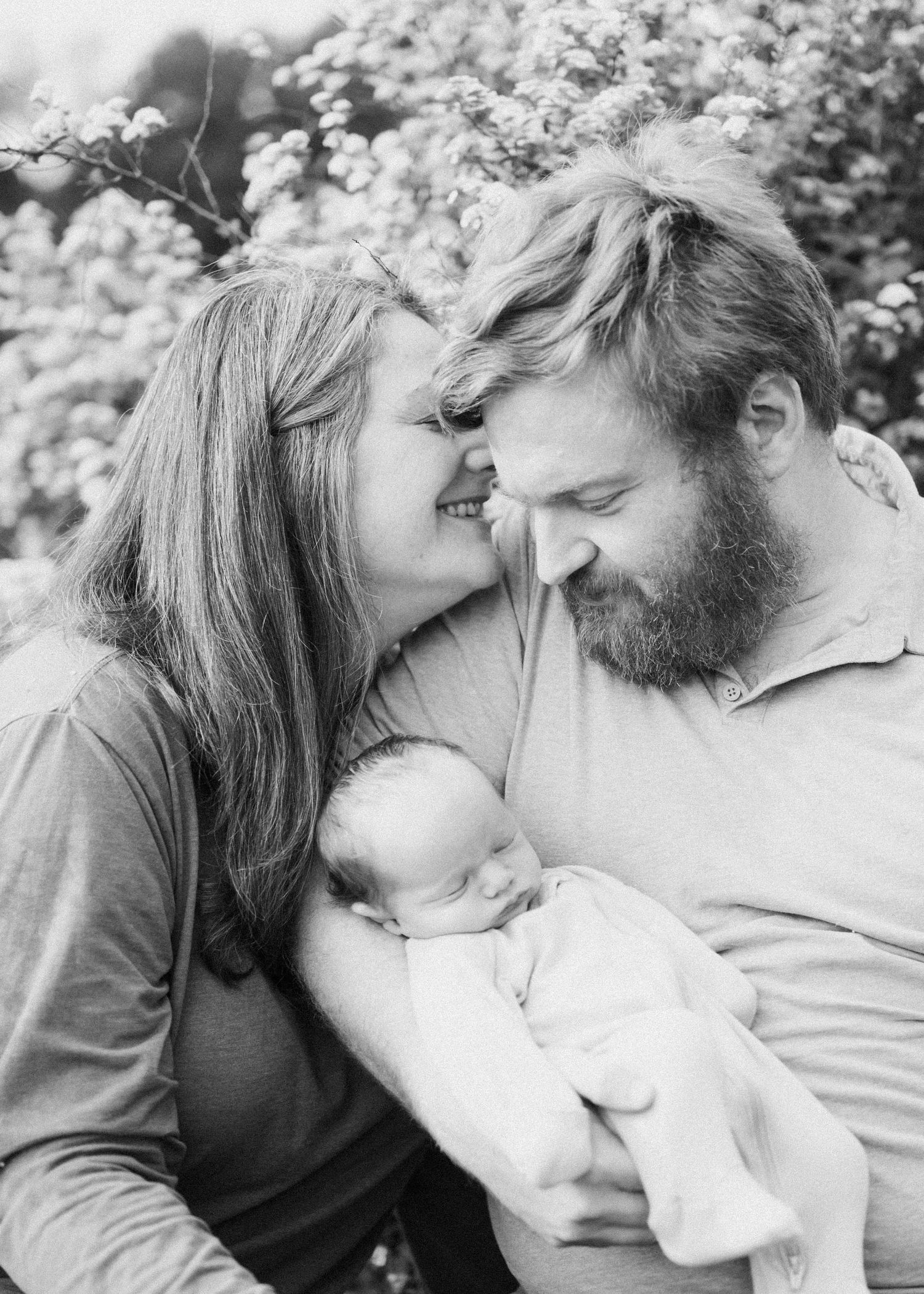 Black and white photo of parents smiling at their sleeping newborn. Minneapolis Newborn Photography.