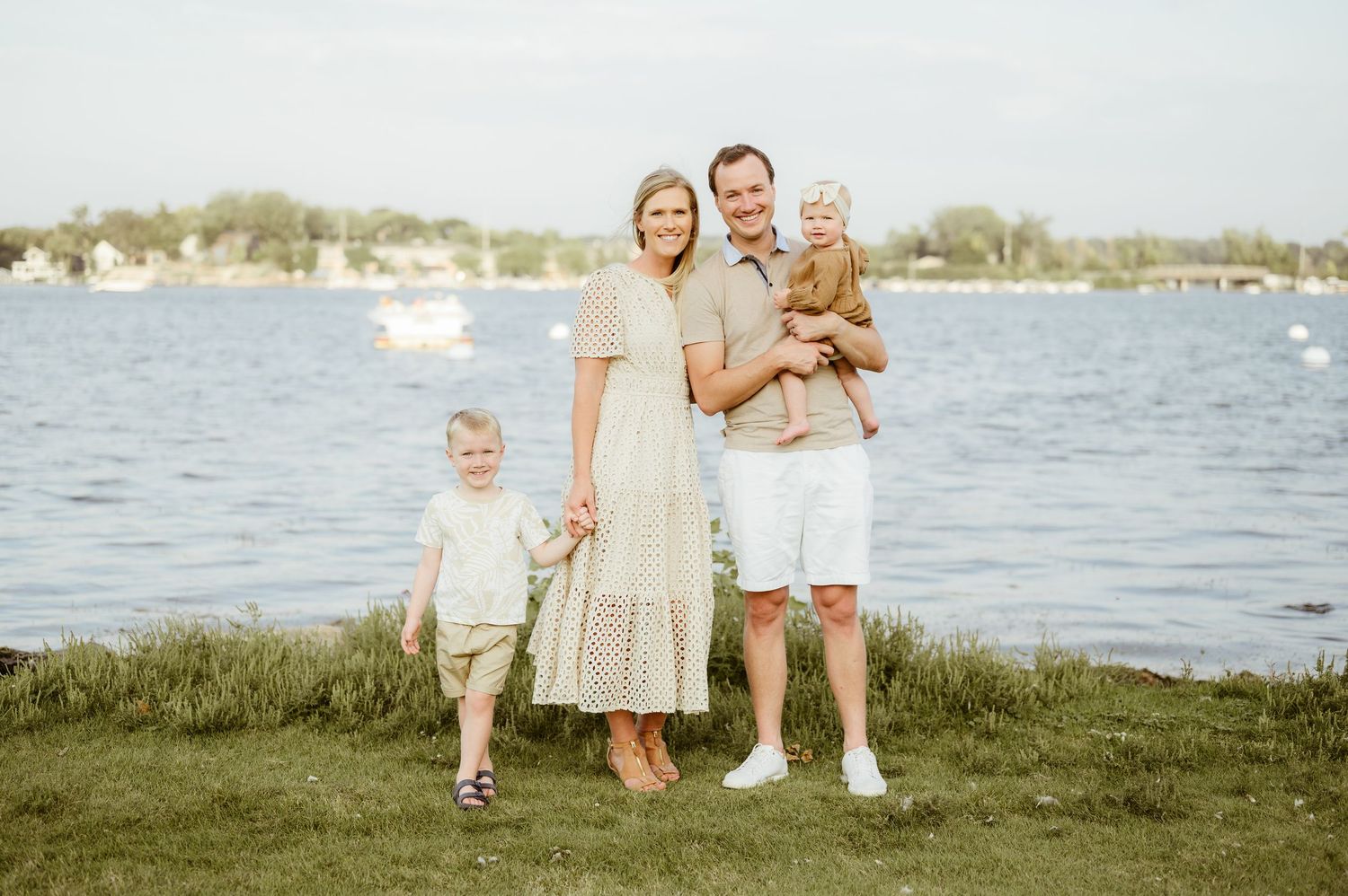 A happy family of four poses together by a lakeside on a sunny day.
