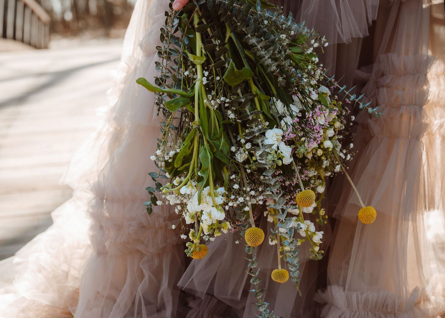 Bride holding a wildflower bouquet with yellow billy balls and white blooms against a ruffled tulle gown.