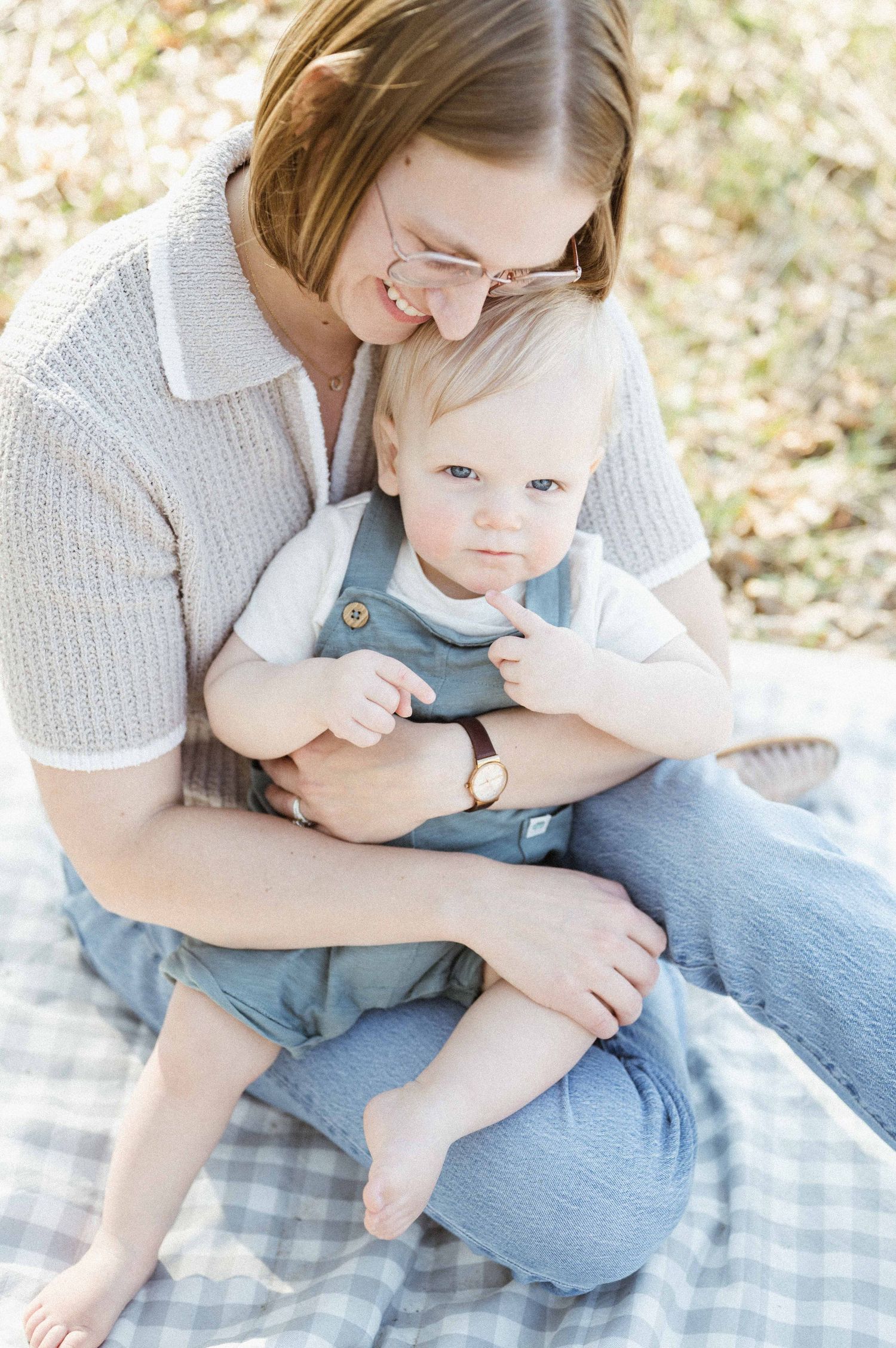 Mother holding her baby boy in blue overalls on a checkered blanket. St. Paul Family Photographer.