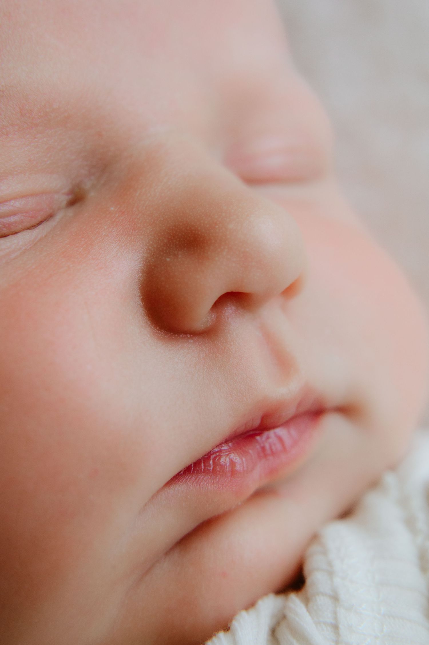 Close-up of a sleeping newborn baby's face with soft skin, tiny nose, and delicate pink lips.
