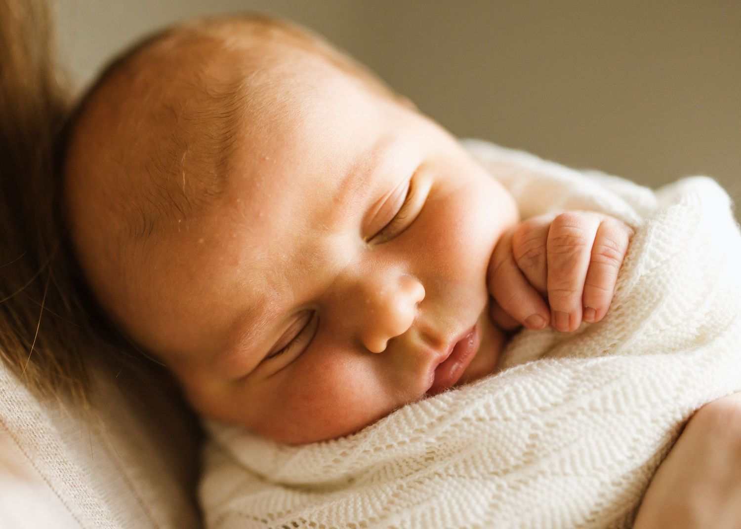 Peaceful newborn baby sleeping wrapped in a soft white knit blanket, cradled in loving arms.