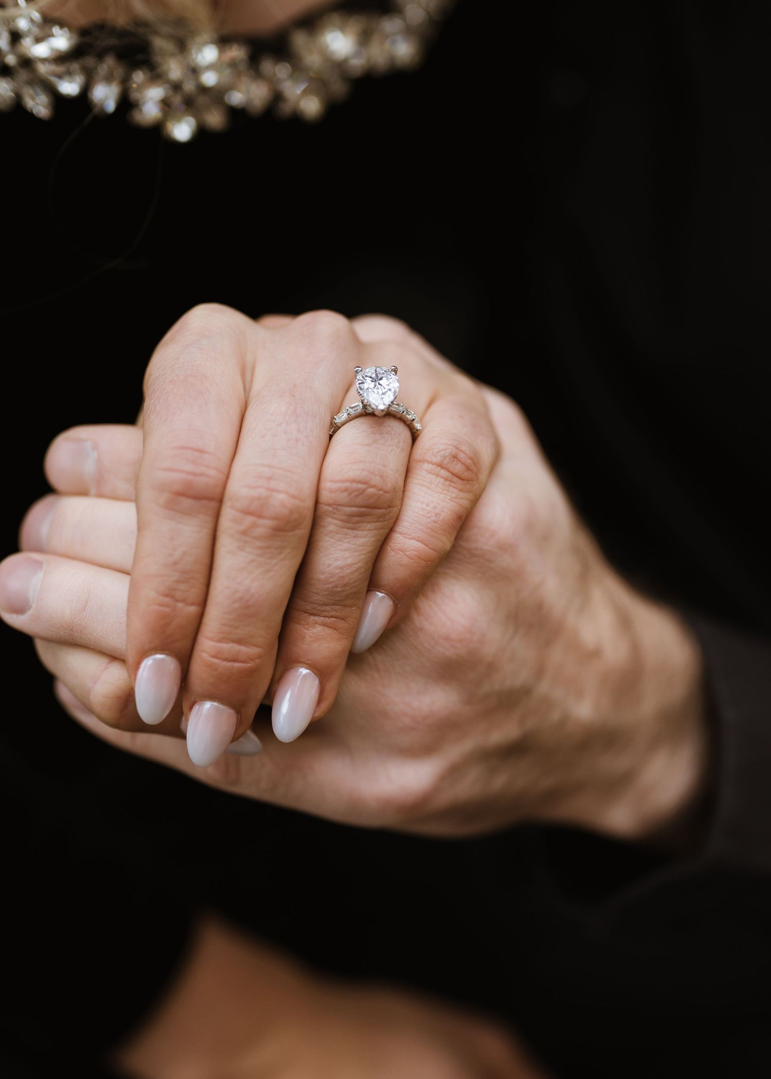 Close-up of a woman's hands wearing a large diamond solitaire engagement ring with nude manicured nails.