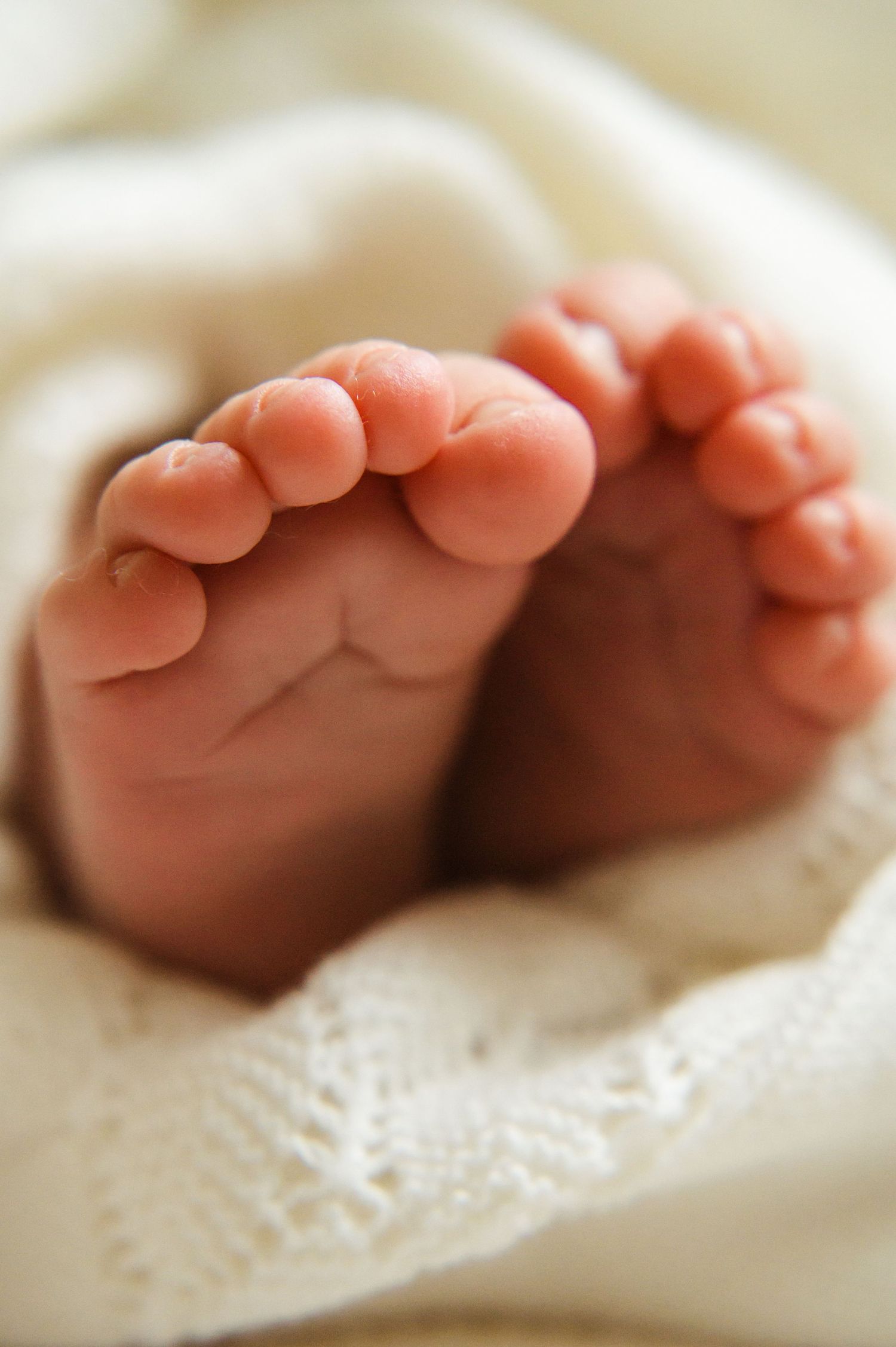 Close-up of tiny newborn baby feet peeking out from soft white knit blanket.