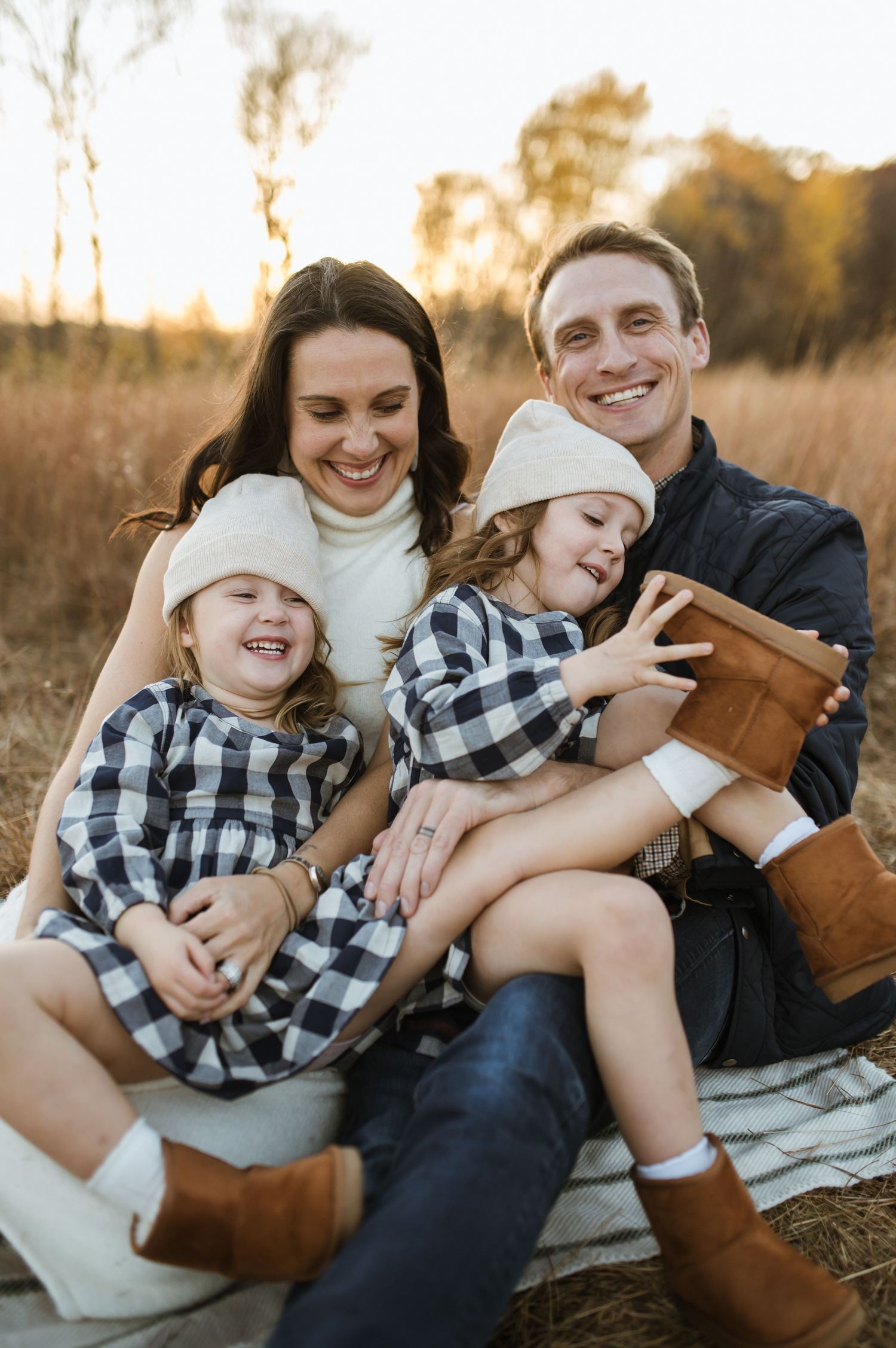 Happy family sitting together in a sunlit fall field, children holding a book with parents smiling.