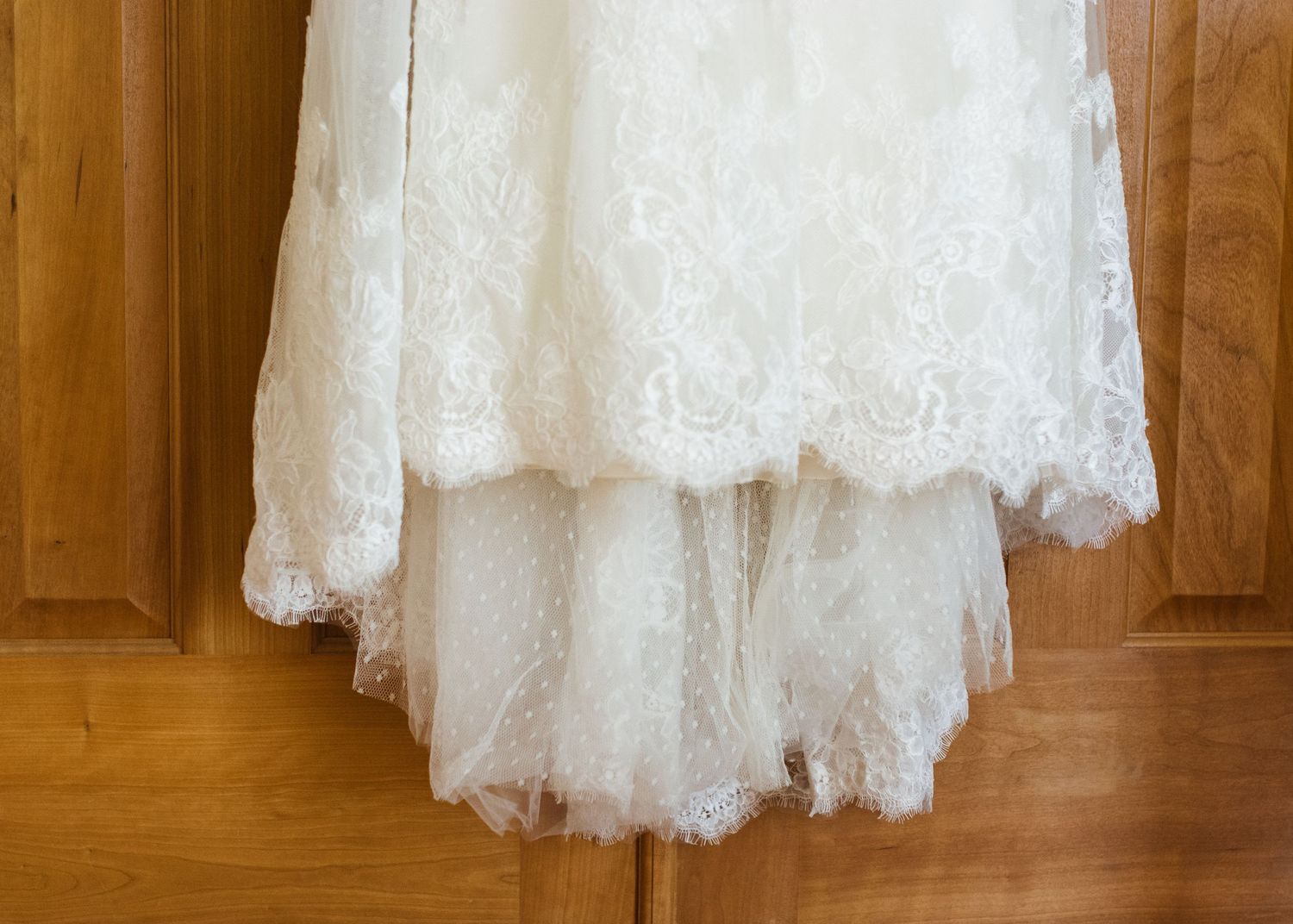 Elegant lace and tulle wedding dress with scalloped hem hanging on wooden door.
