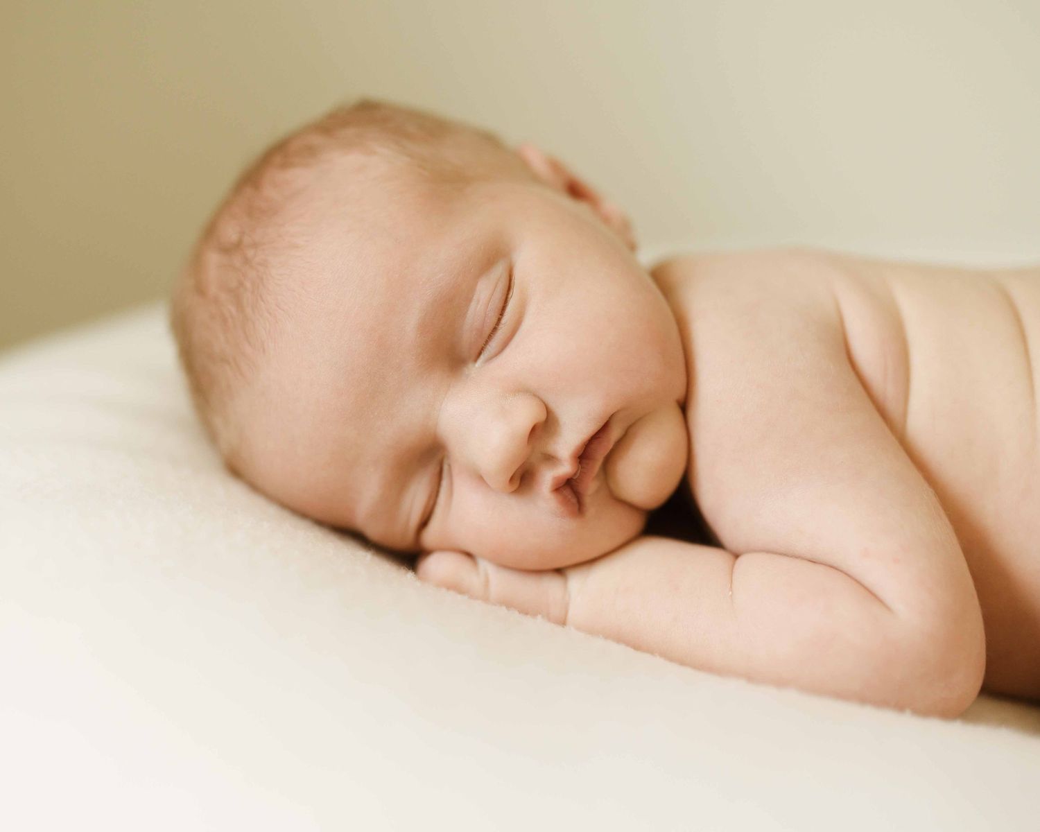 Serene newborn baby sleeping on a white surface, curled up in a natural fetal position.