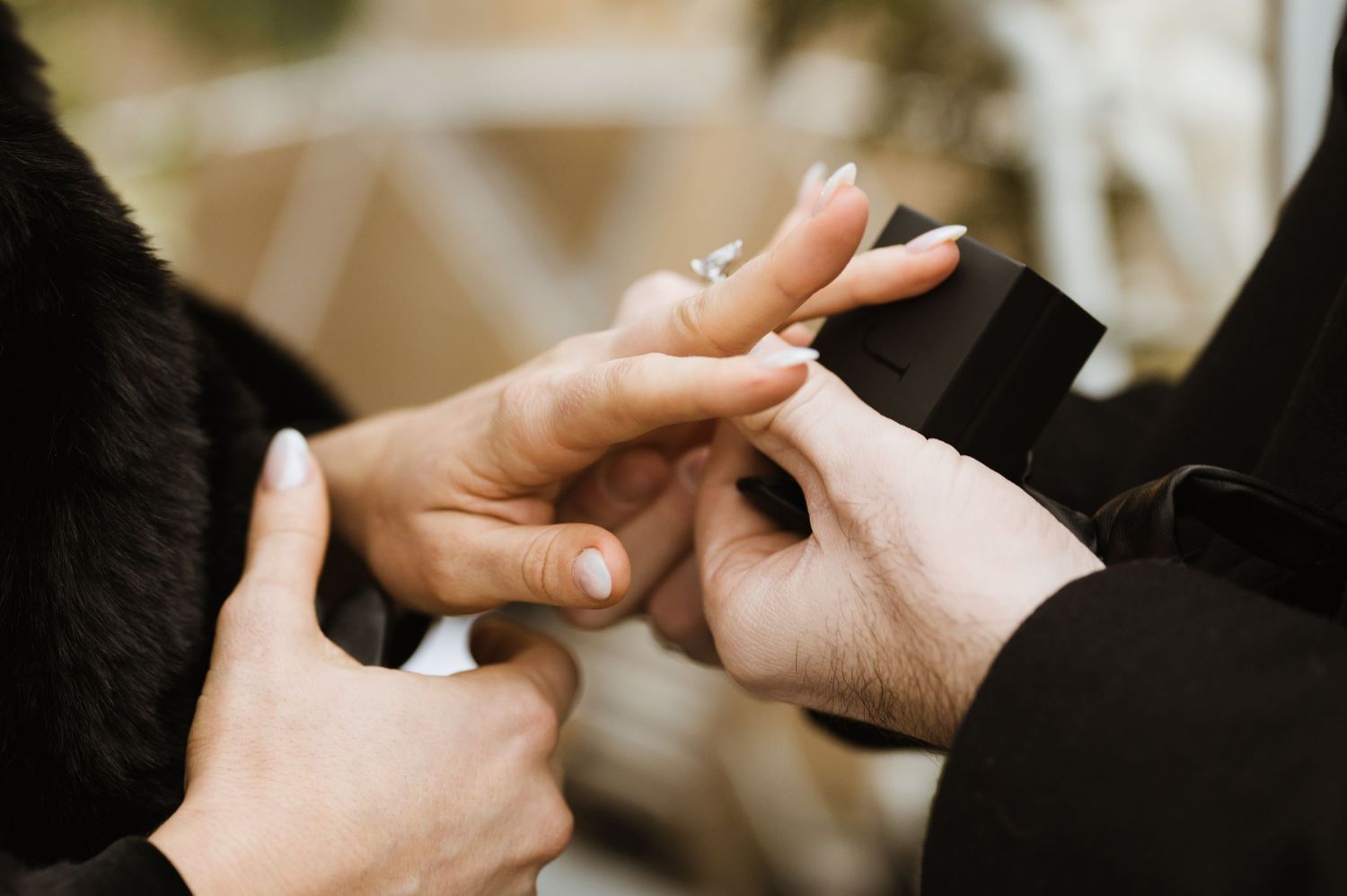 Close-up of hands placing a diamond engagement ring on a finger during a proposal.