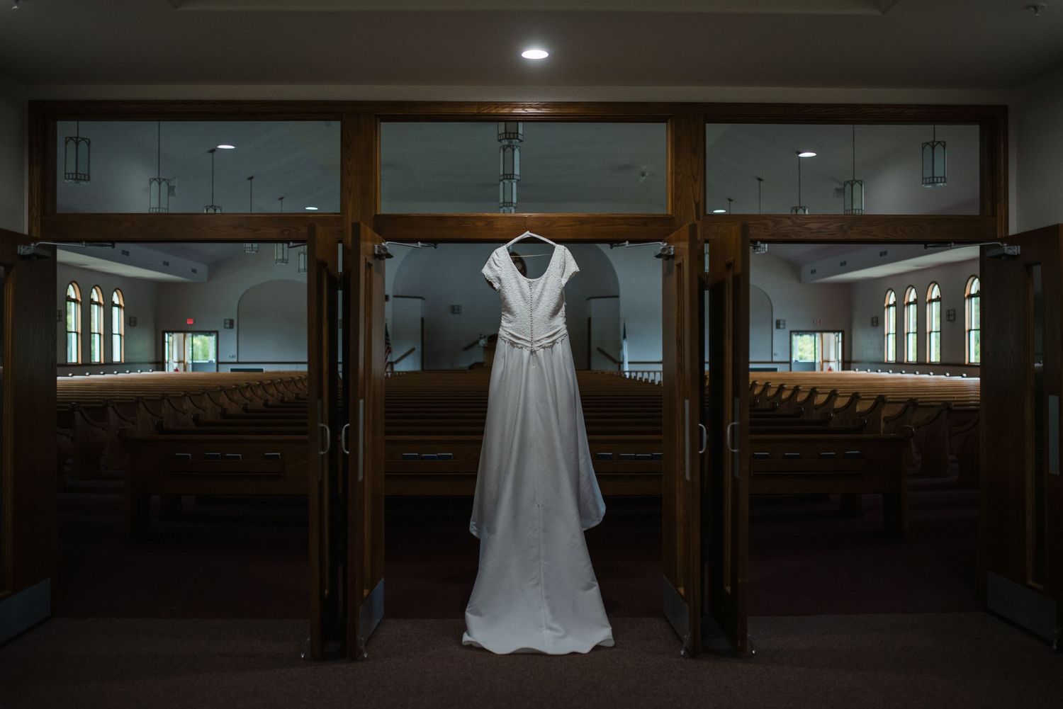 Elegant white wedding dress hanging in church doorway with wooden pews visible in background.
