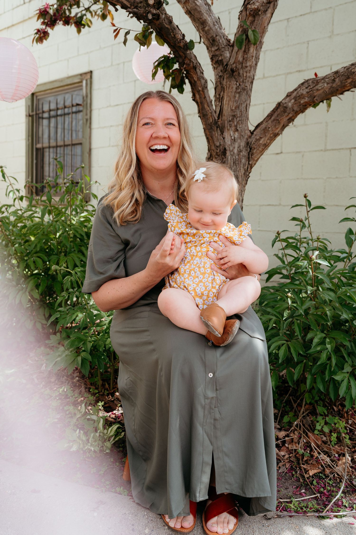 Laughing mother holding her smiling baby girl outdoors near a tree. Minneapolis Photographer.