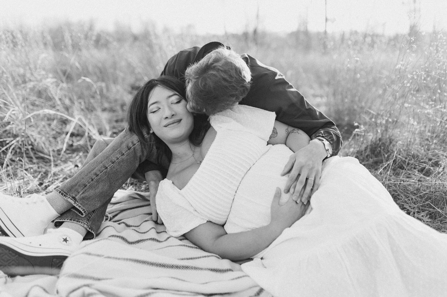 Black and white photo of child hugging his mother lying in a field. Minneapolis Maternity Photographer