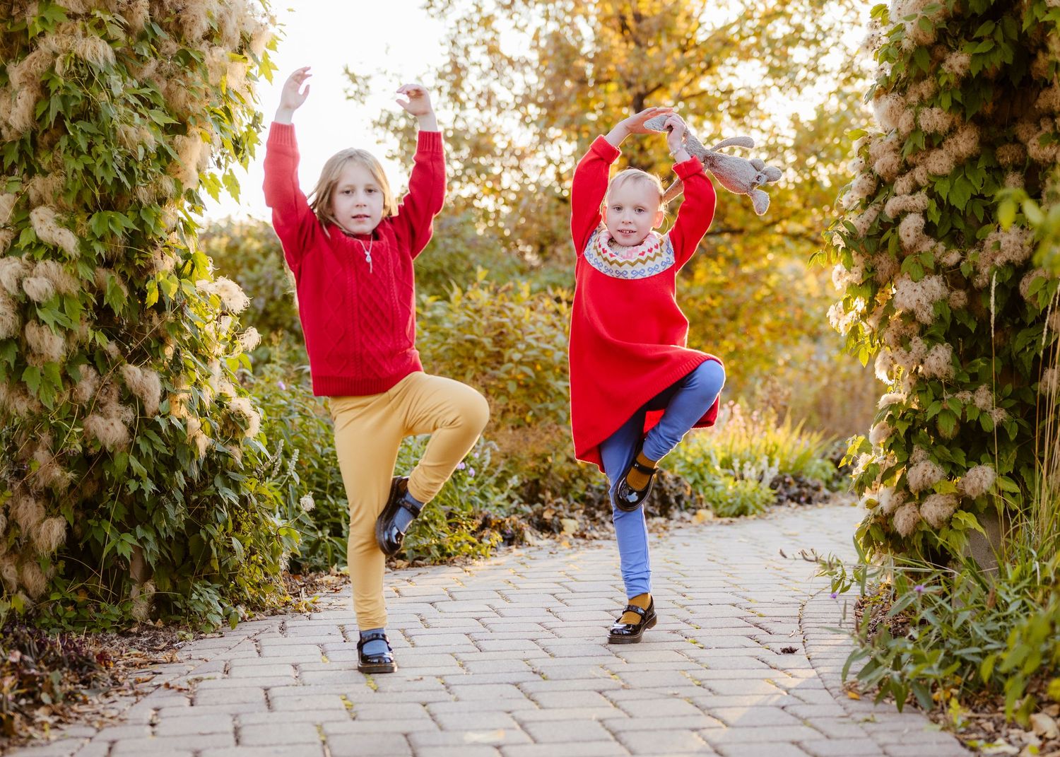 Two joyful children in red and yellow outfits jumping with arms raised in an autumn garden.