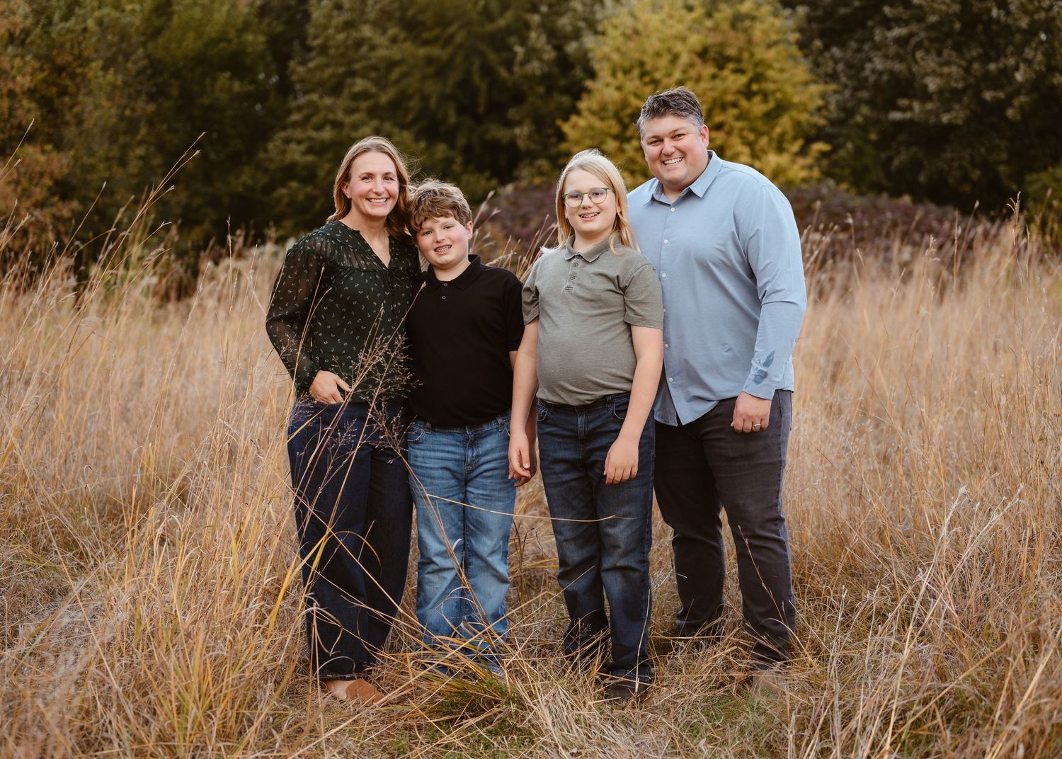 Family of four smiling together in a golden field during a fall outdoor portrait photography session.