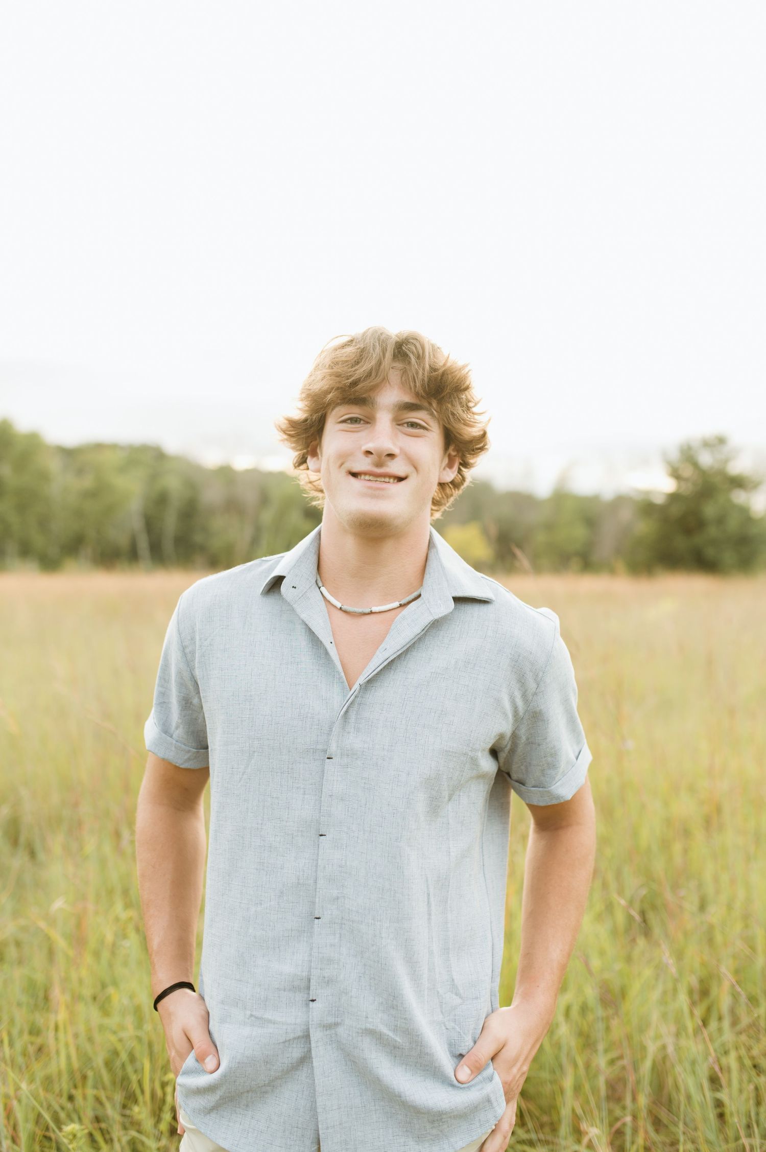 Young man in gray short-sleeve shirt standing in a golden grass field smiling.