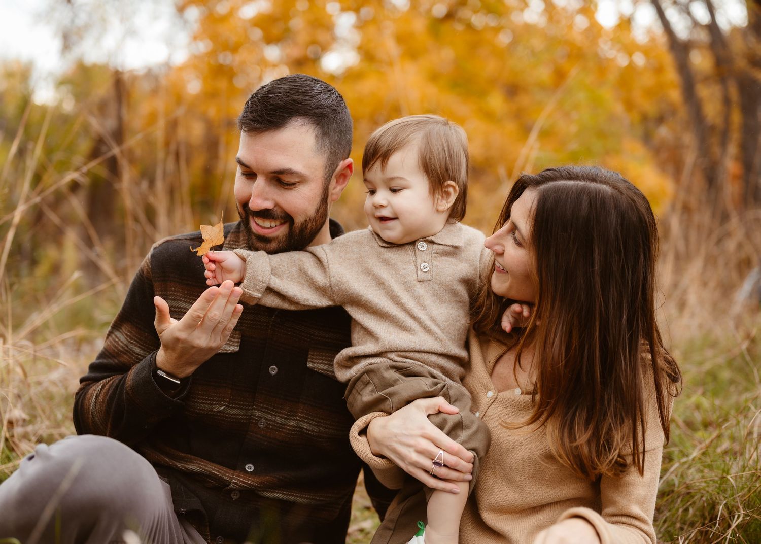 A joyful young family with a baby enjoys autumn outdoors, surrounded by golden foliage. Minnesota Family Photographer