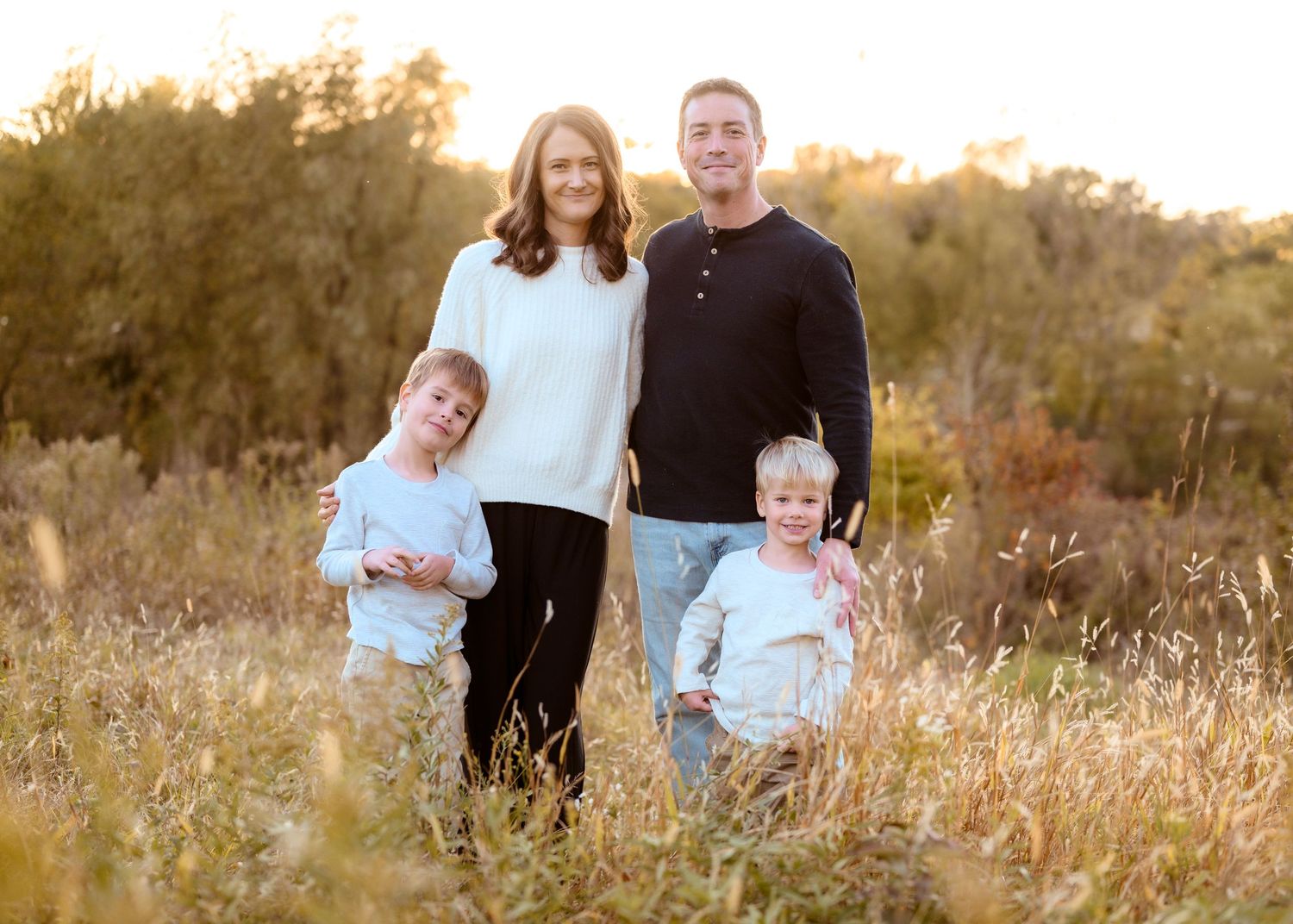 Happy family of four posing in a sunlit golden field during a warm autumn family portrait session.
