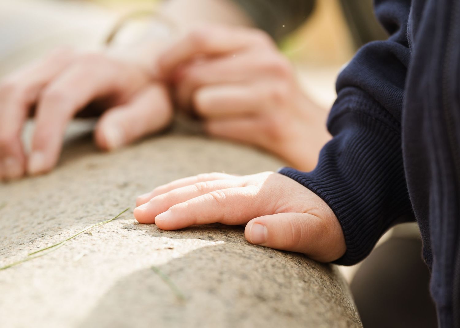 Close-up of a small child's hand and adult hand resting together on a stone surface outdoors.