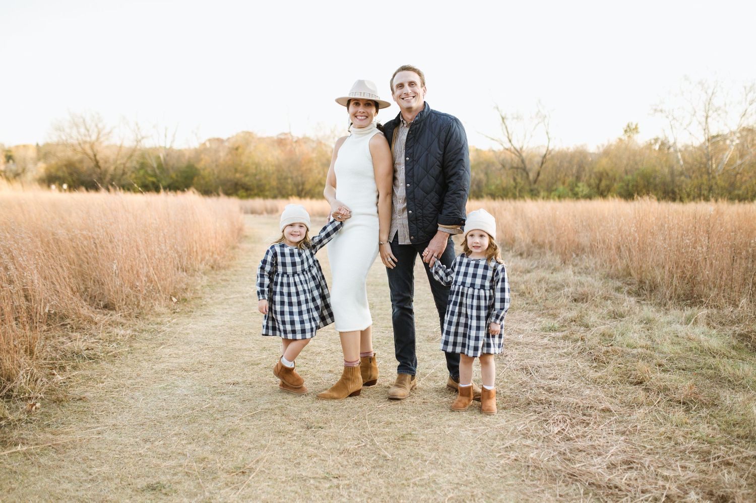 Family of four smiling on a dirt path in a golden field during fall.