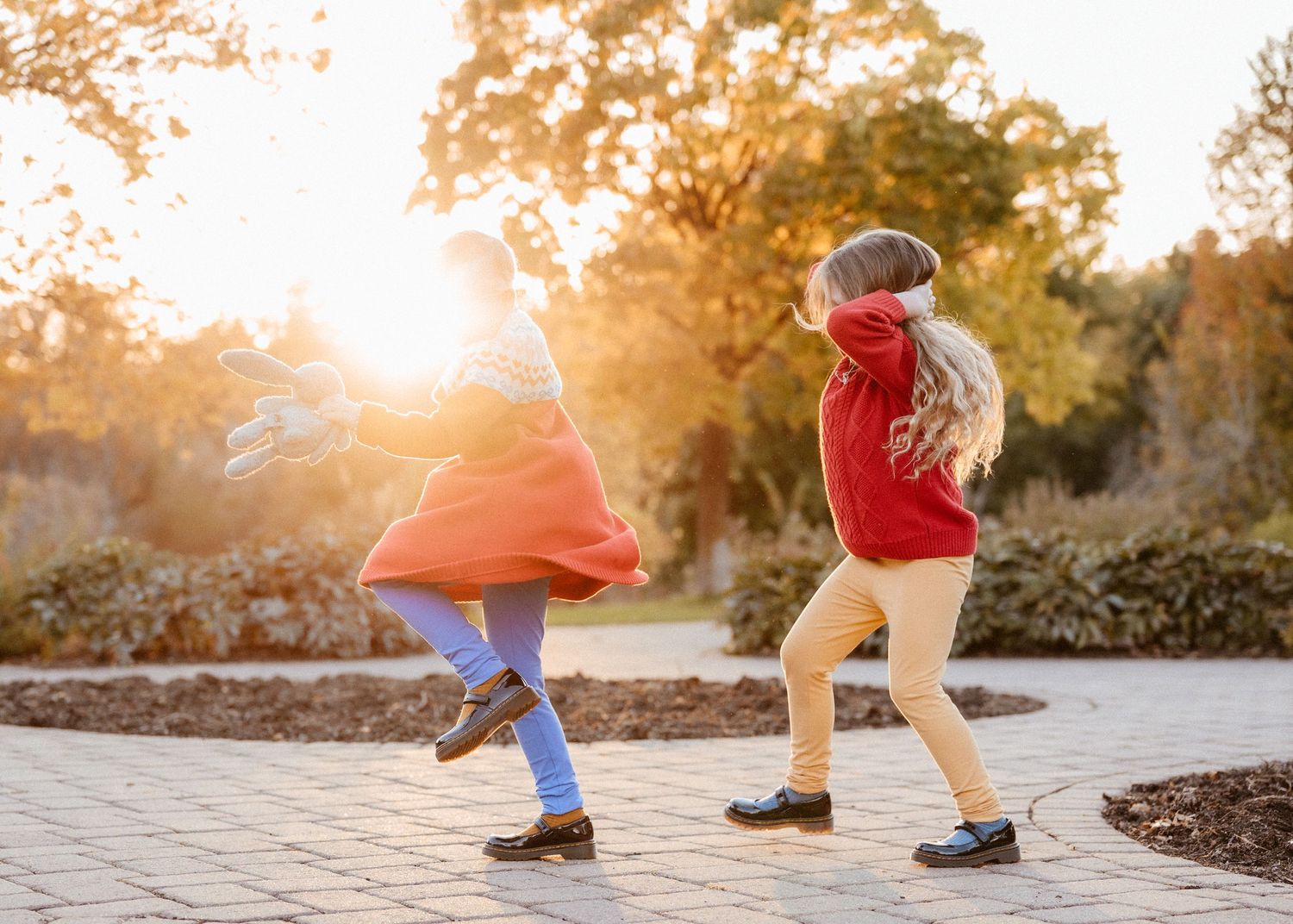 Two children dancing and spinning on a brick path in a sunlit autumn garden.