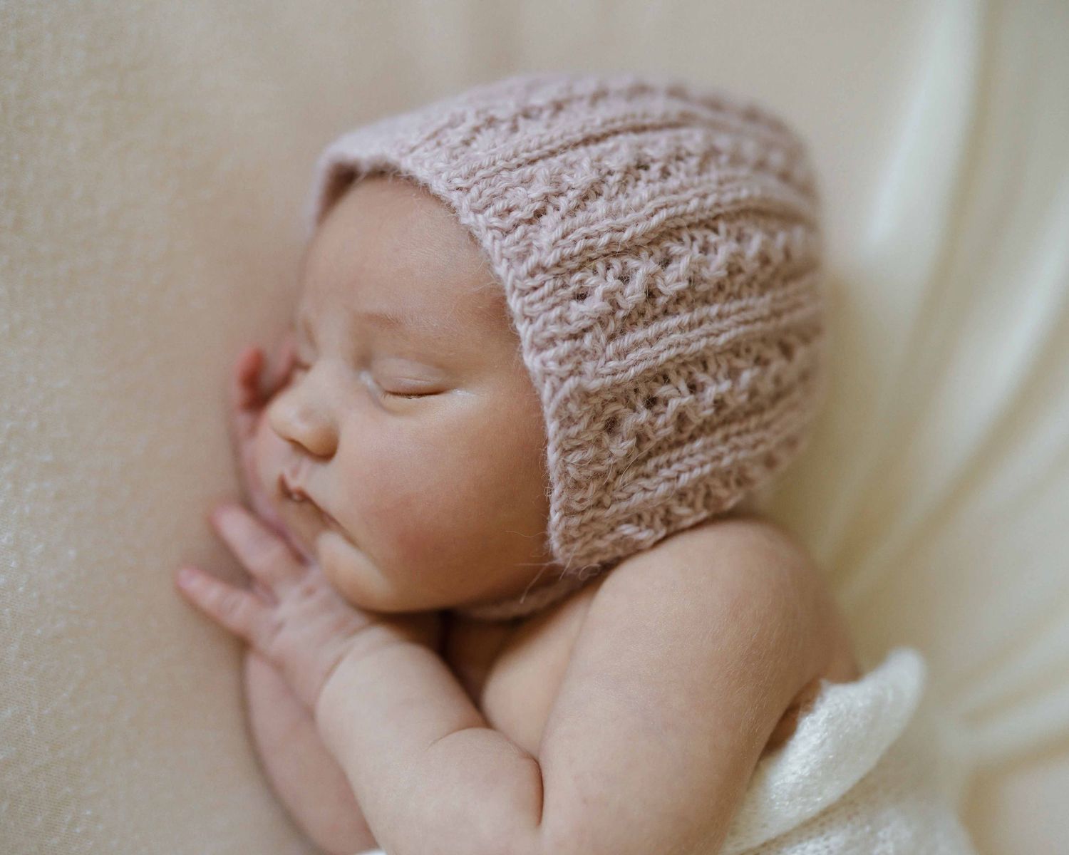 Adorable newborn baby wearing a pink knitted bonnet, peacefully sleeping with tiny hands together.