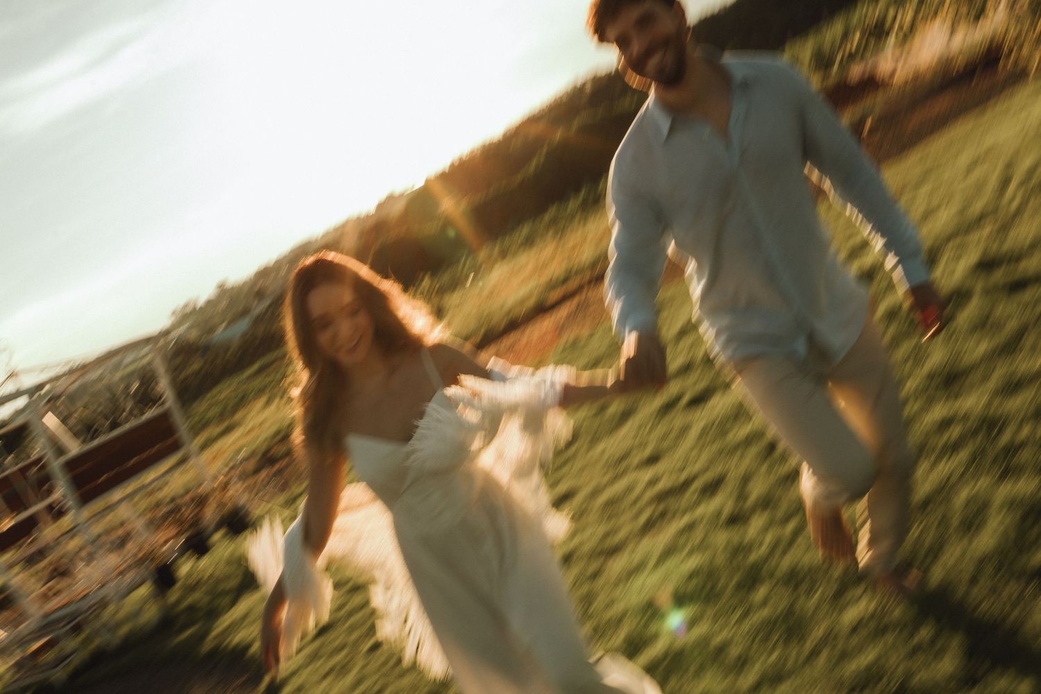 Blurred motion photo of couple holding hands running through sunlit green field at sunset.