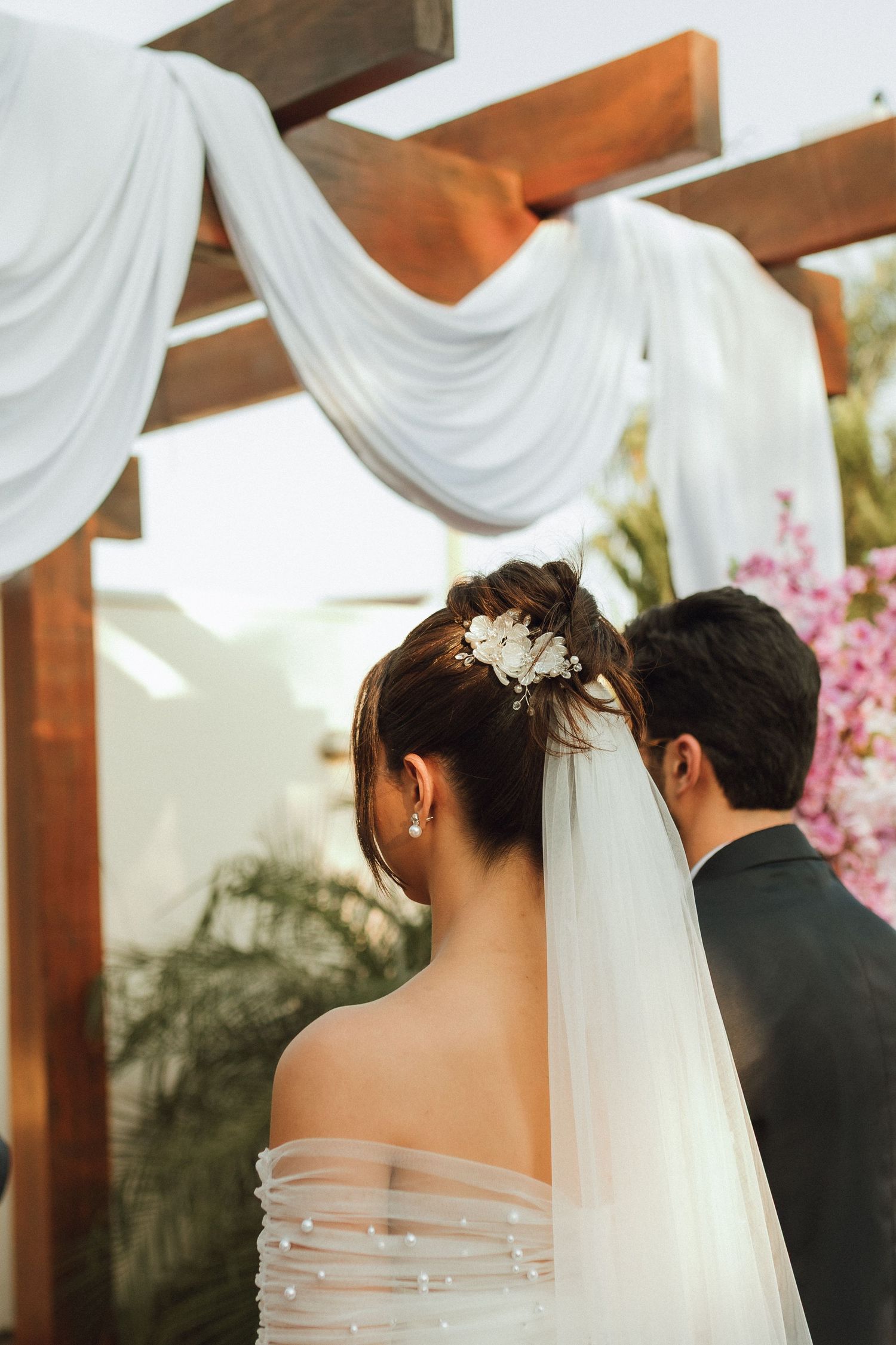 Close-up of bride's elegant updo with floral hair accessory and veil at outdoor ceremony.
