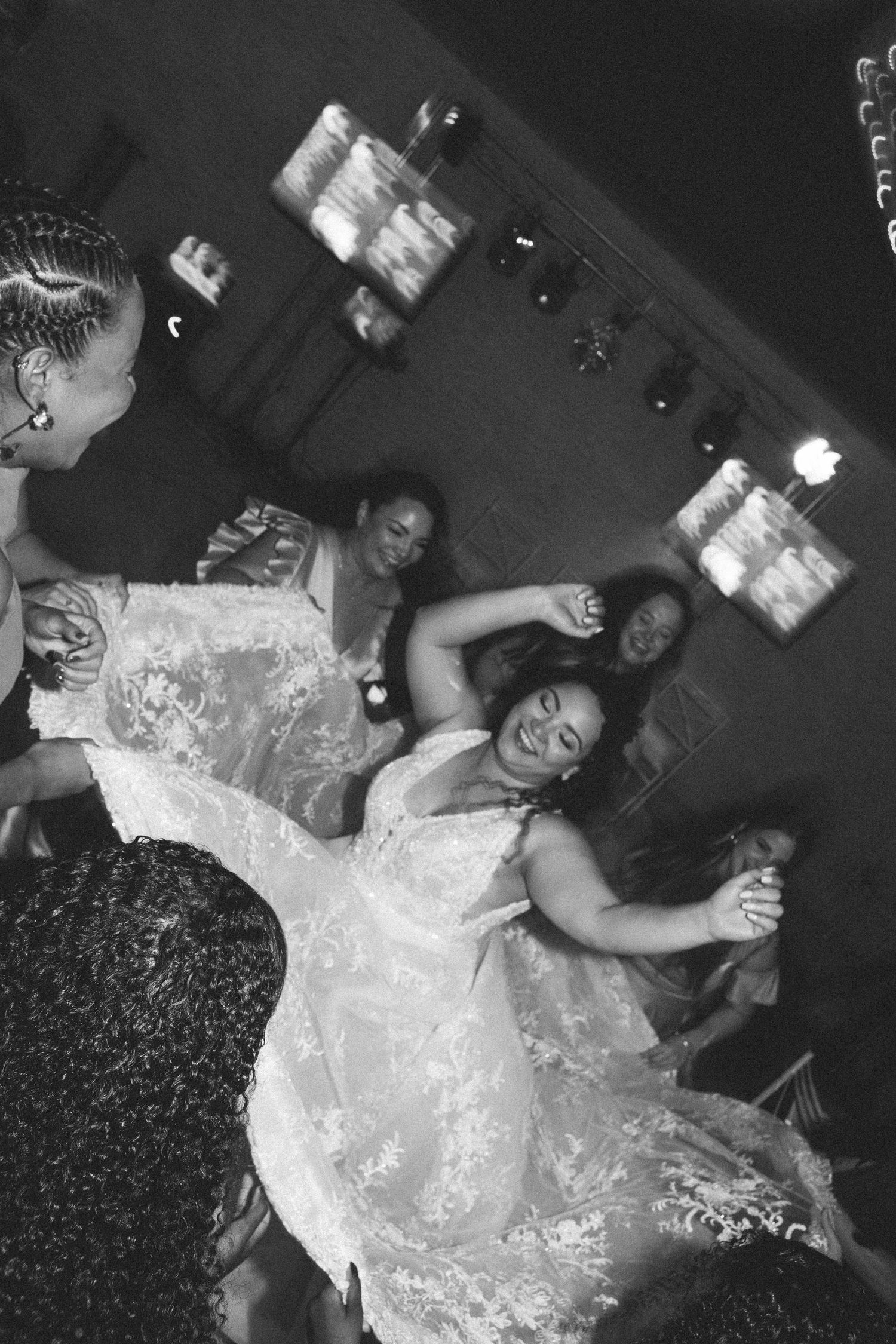Black and white photo of bride dancing joyfully on the dance floor with guests at wedding reception.