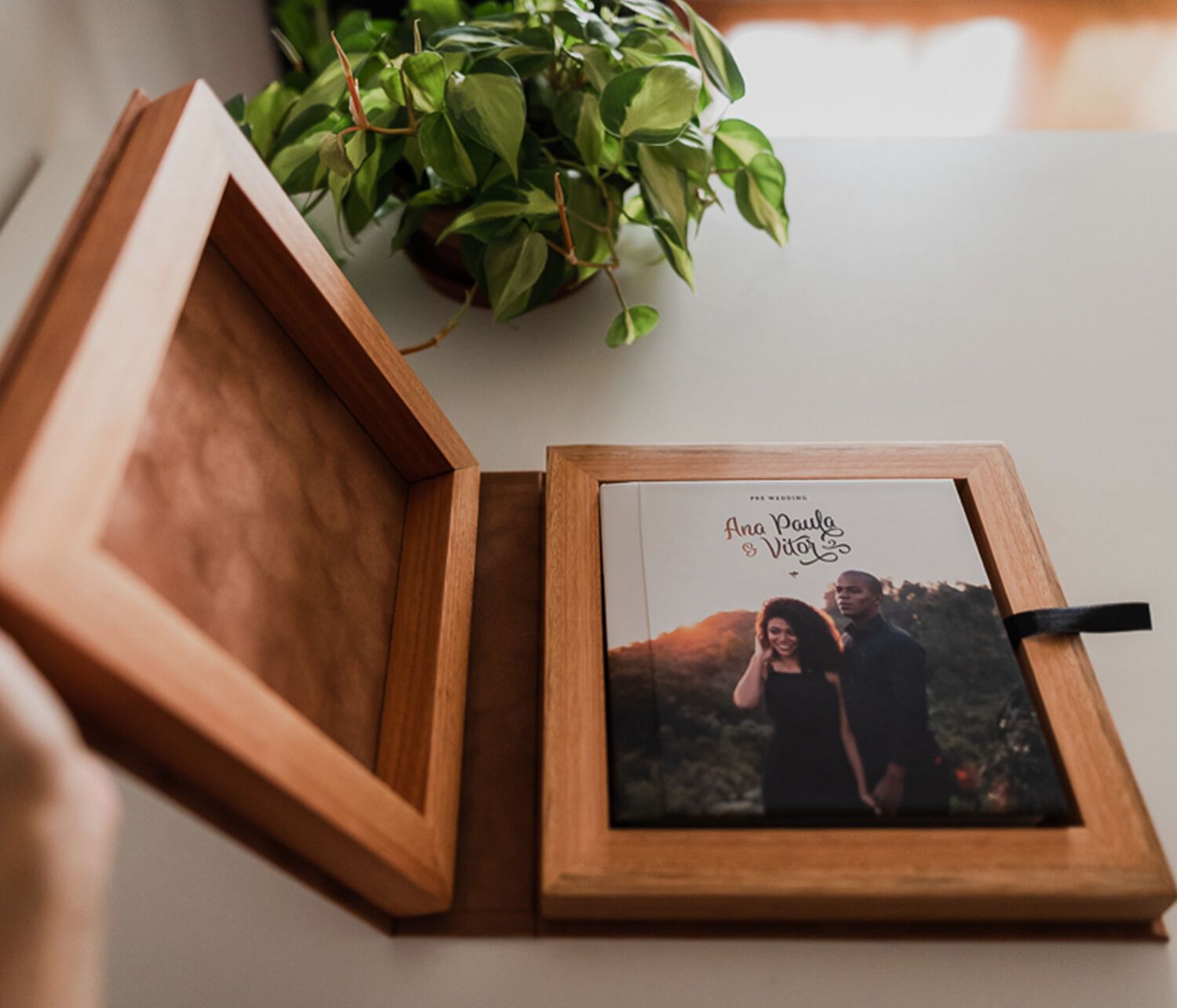 Wooden keepsake box open displaying a wedding photo album with couple portrait on white table near green plant.