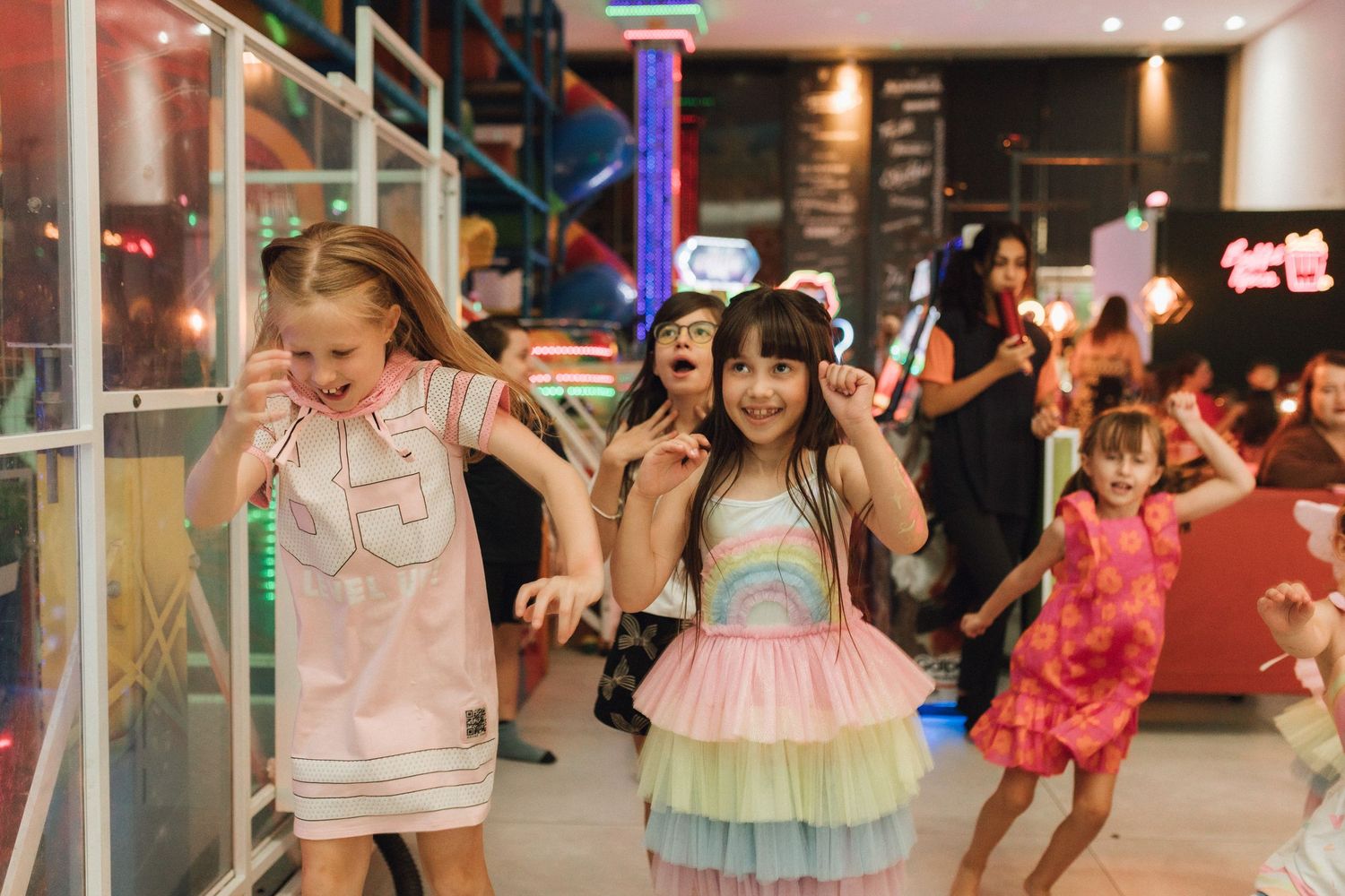 Children dancing and laughing at a colorful indoor party venue, wearing festive dresses in a fun celebration.